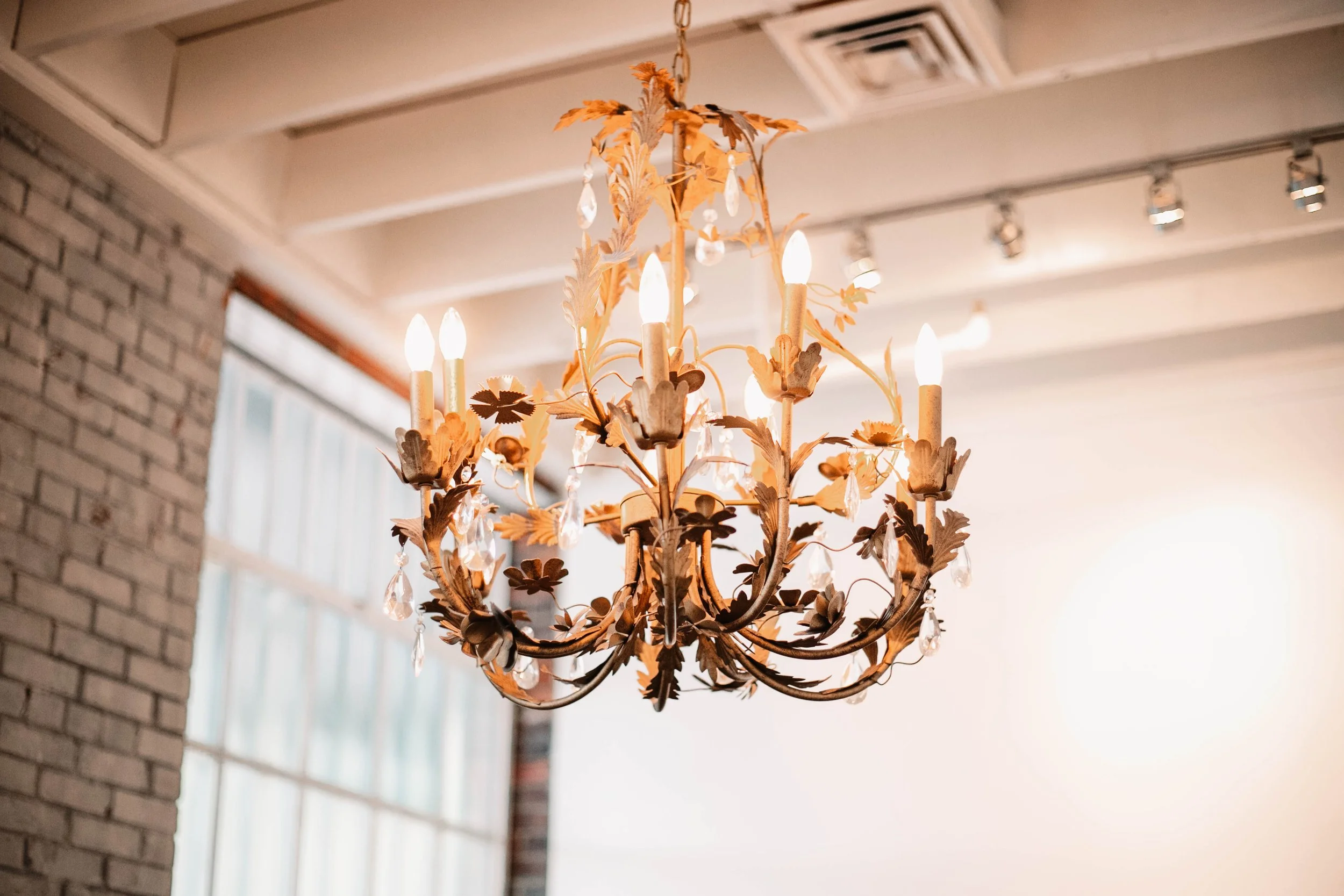 Elegant chandelier with candle-shaped lights, decorative leaves, and hanging crystals in a bright room.