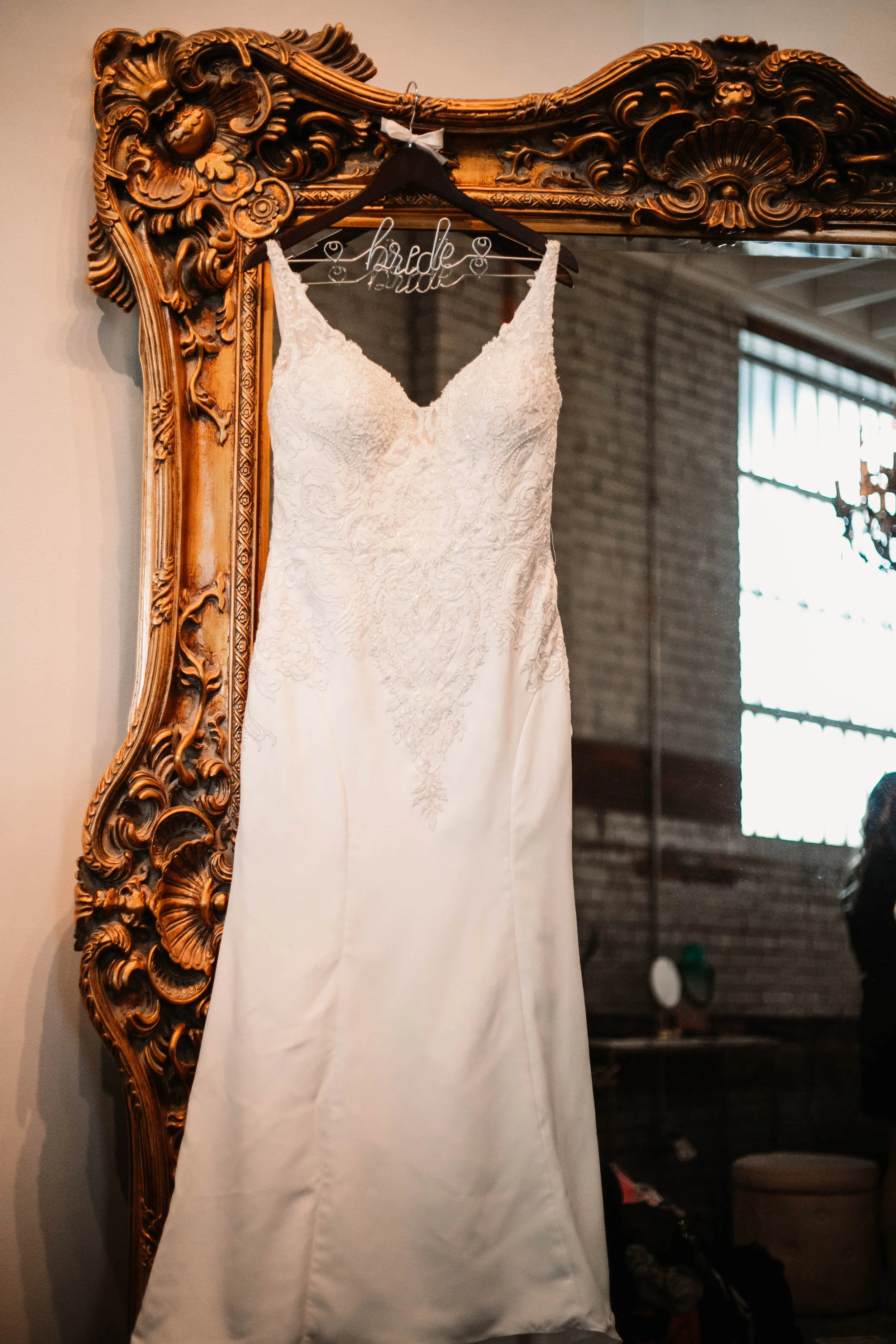 Wedding dress hanging on a decorative wooden mirror with a 'bride' wire hanger.