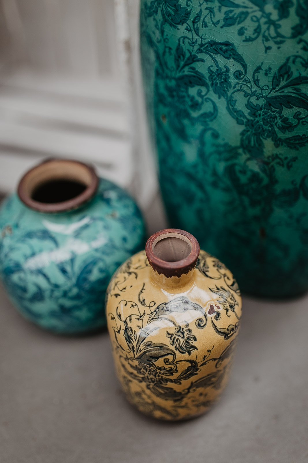 Drei Keramikvasen mit floralen Mustern, zwei in Türkis und eine in Gelb.