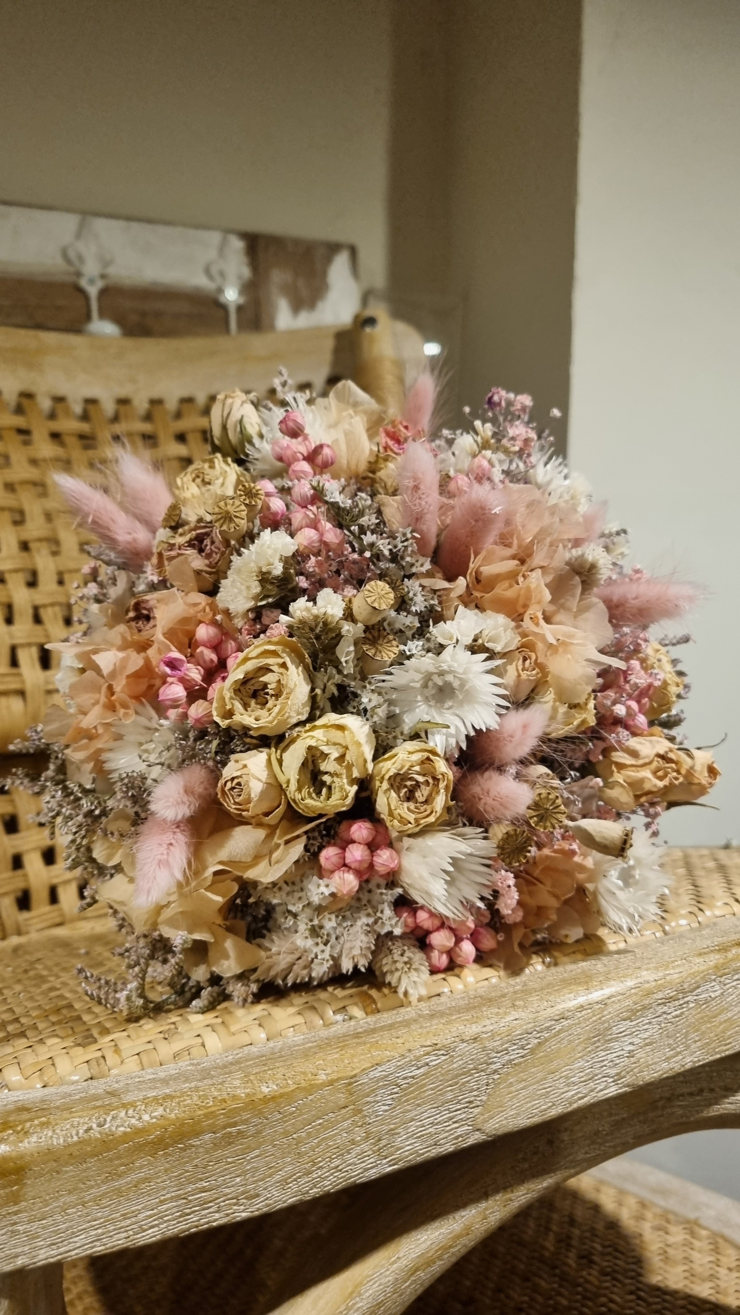 Trockenblumenstrauß auf einem Stuhl aus Holz mit Korbgeflecht, bestehend aus rosa, weißen und beige Blüten.
