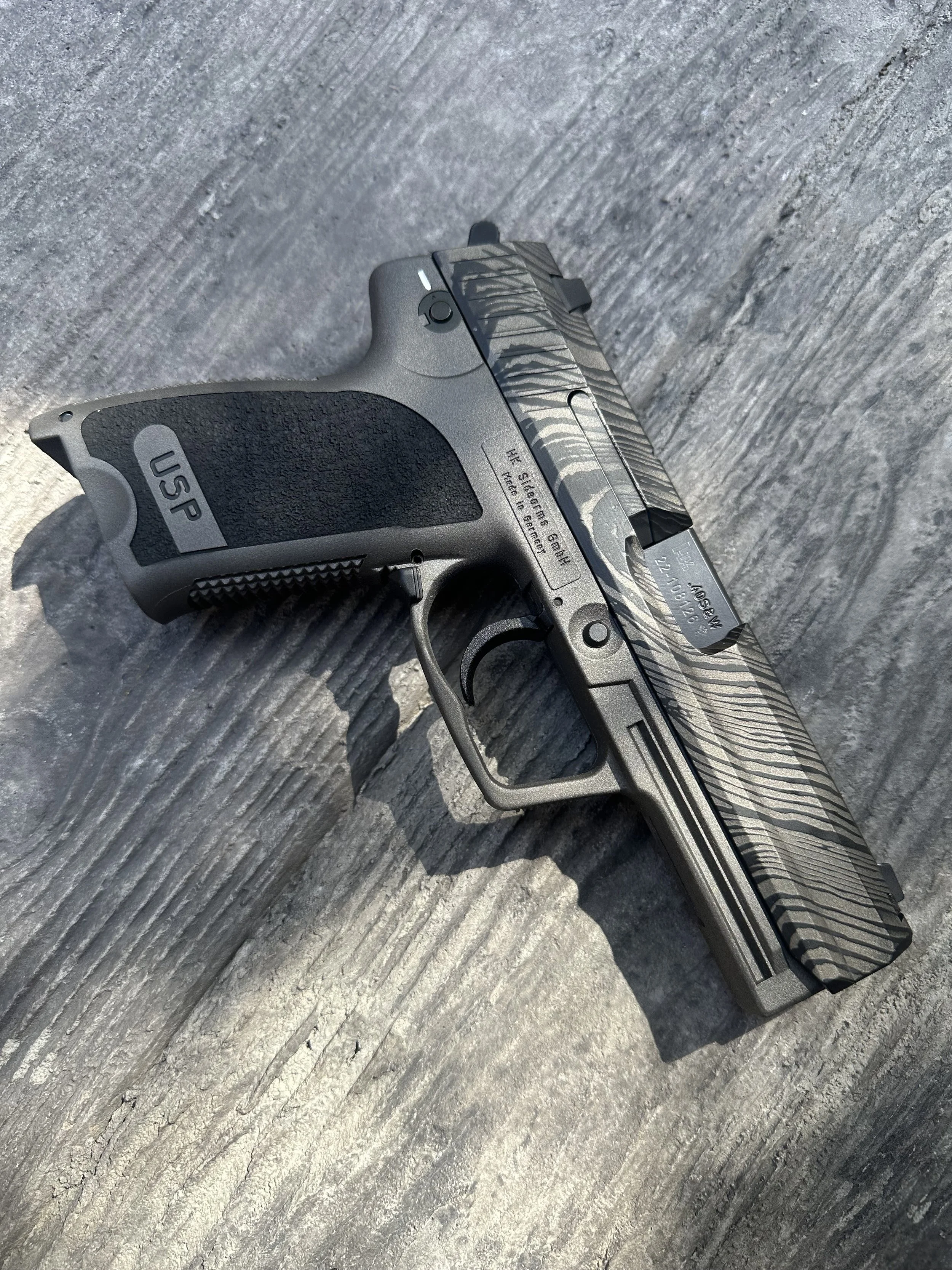 A semi-automatic pistol with a camouflage pattern on the slide, resting on a gray slate surface.