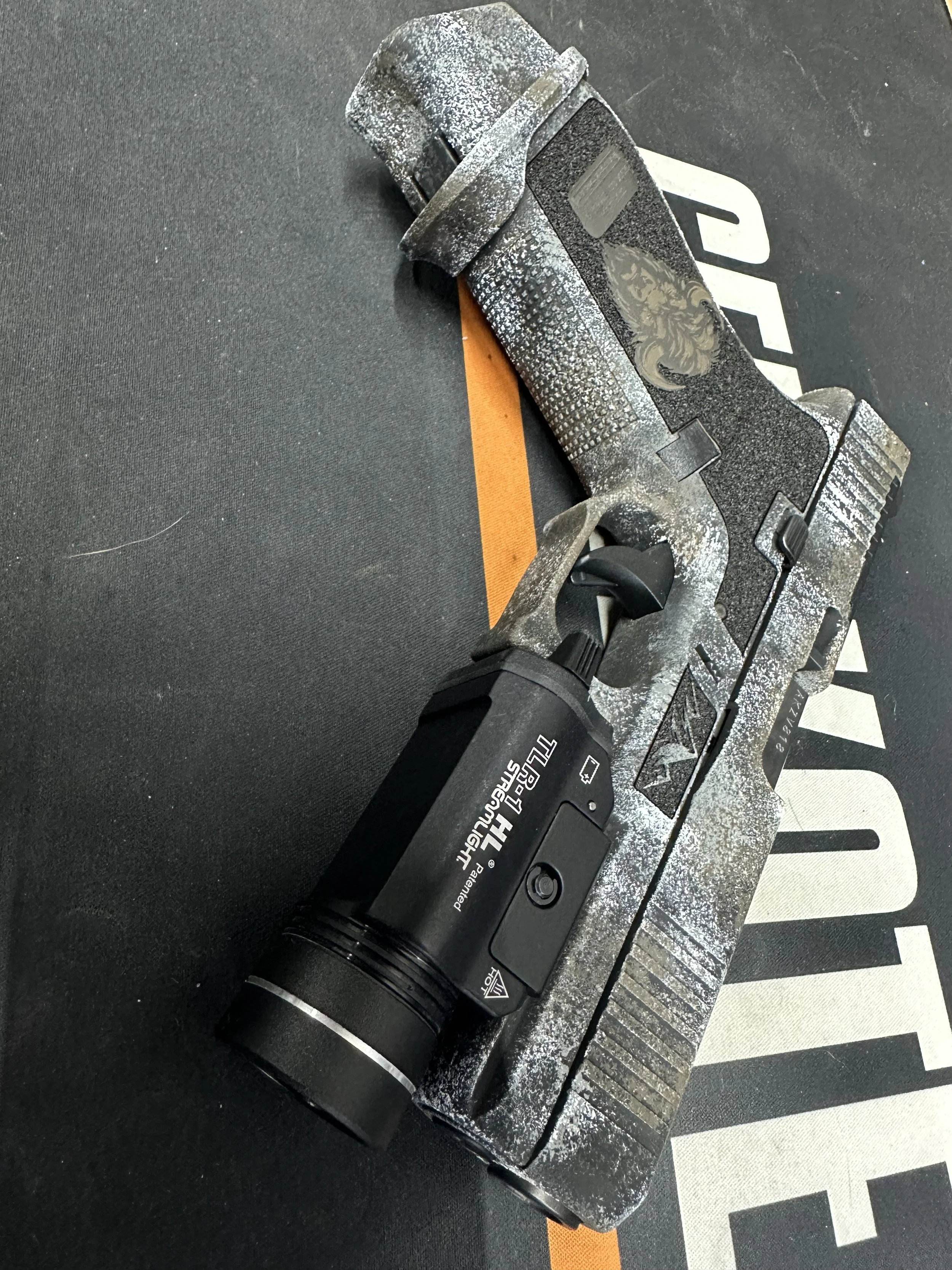 A power drill lying on a black workout mat with a printed logo. The drill is black with a weathered, dusty surface and has a label indicating it is a Hitachi model.