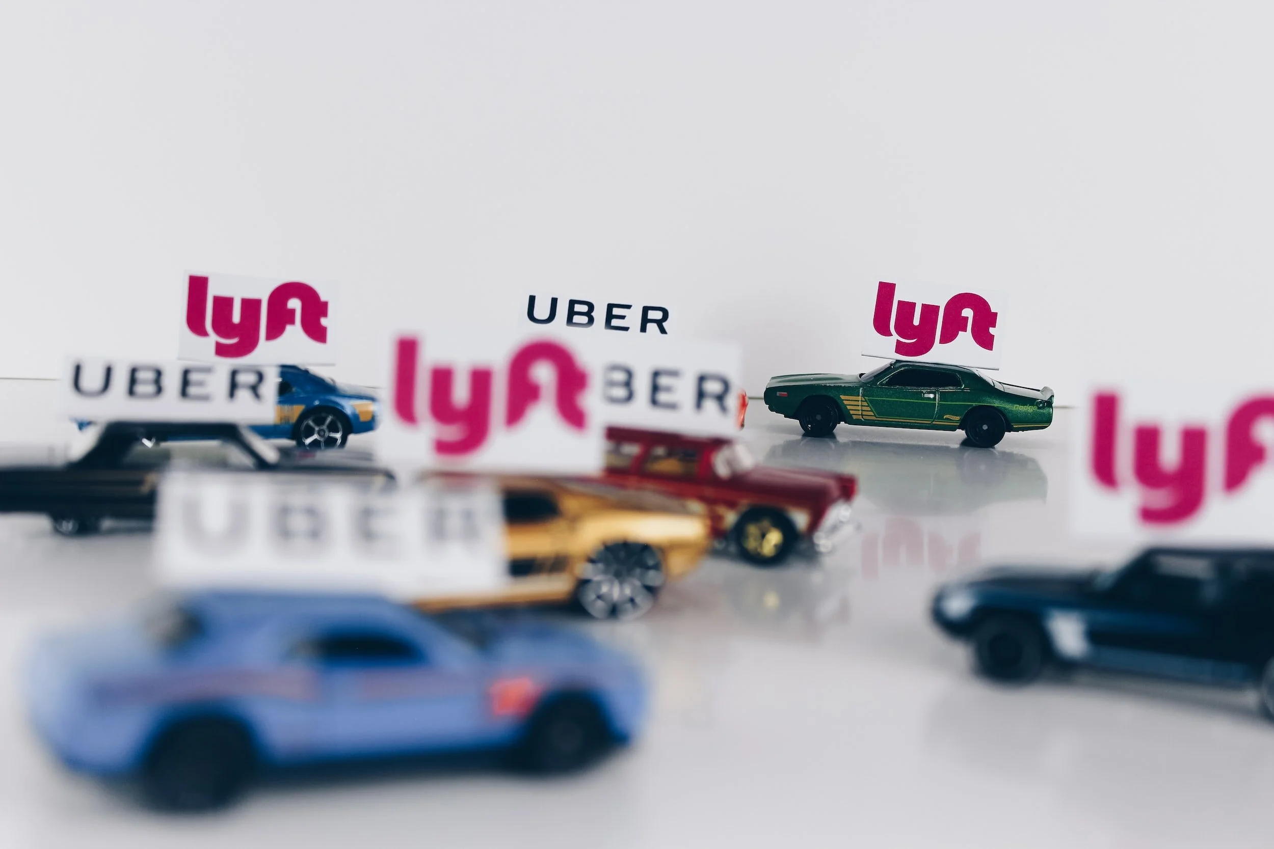 Several toy cars with stickers of Lyft and Uber logos on a white surface.