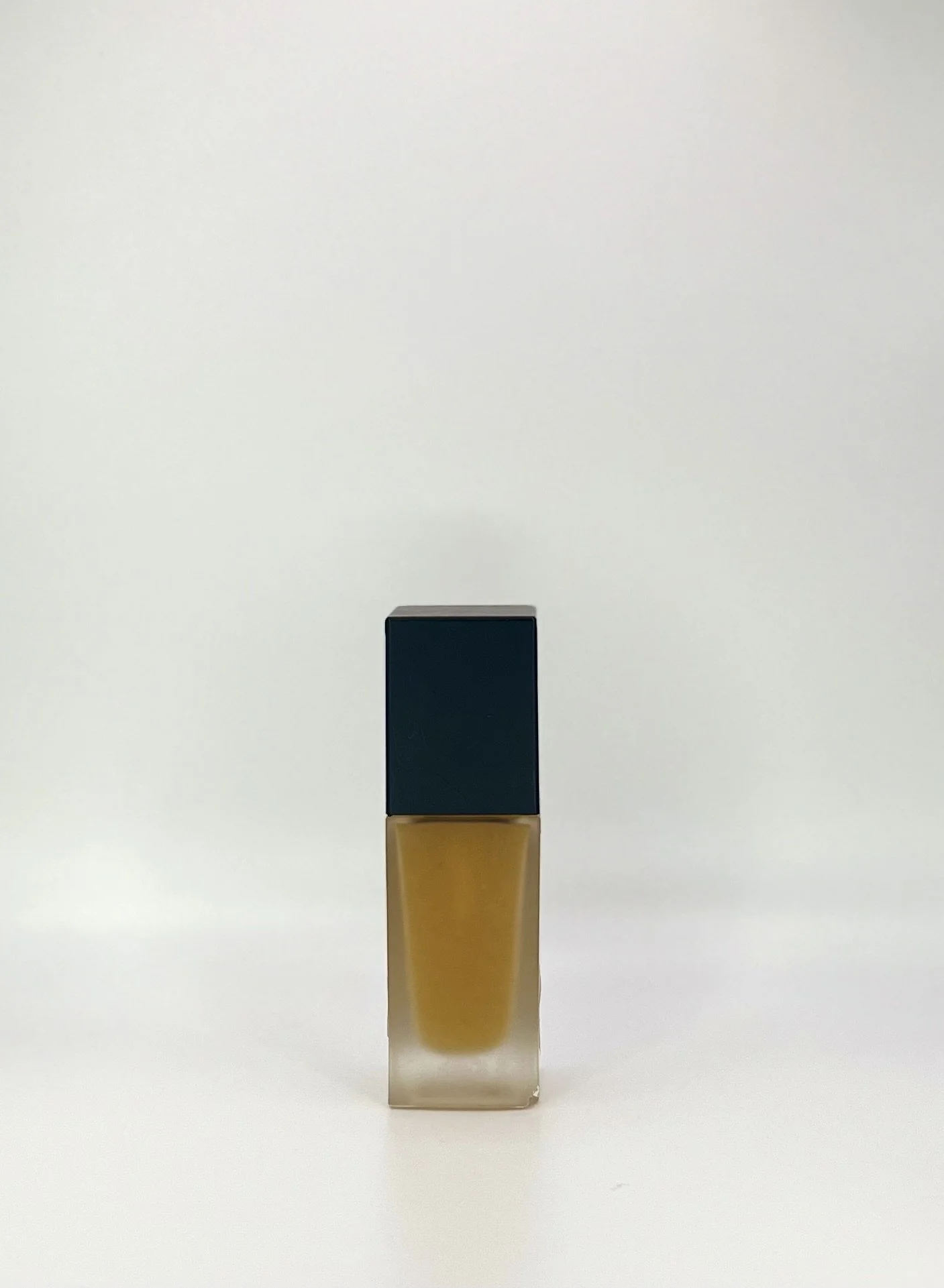 A small bottle of yellow nail polish with a dark blue cap placed on a plain light-colored surface with a neutral background.