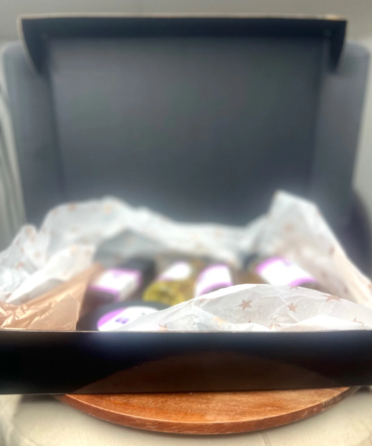 Open black box with wrapped candies inside, sitting on a round wooden tray.