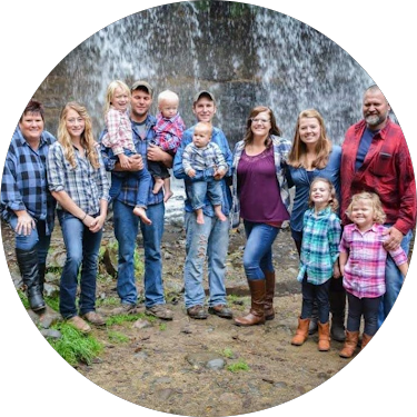 A large family photo taken outdoors in front of a waterfall, with adults and children smiling and standing together.