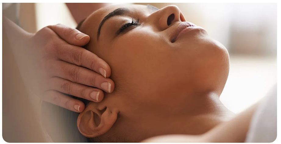 Close-up of a woman receiving a massage or facial on her face by a person with hands on her cheeks.