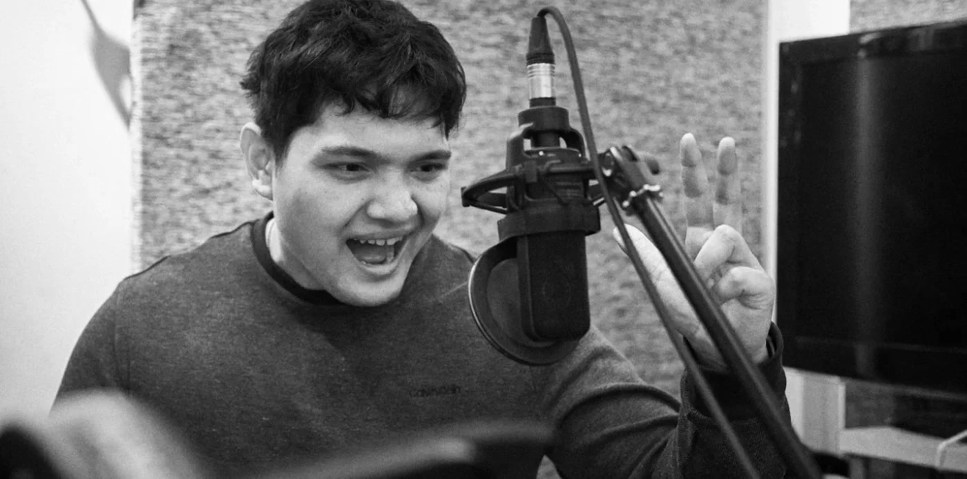 Young man speaking into a studio microphone during a voice-over recording session.