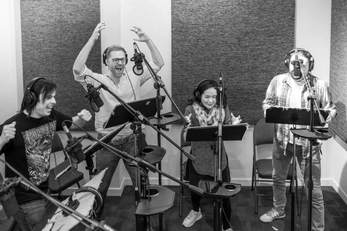 Students performing a group voice-over recording session in a professional studio with microphones and headphones.
