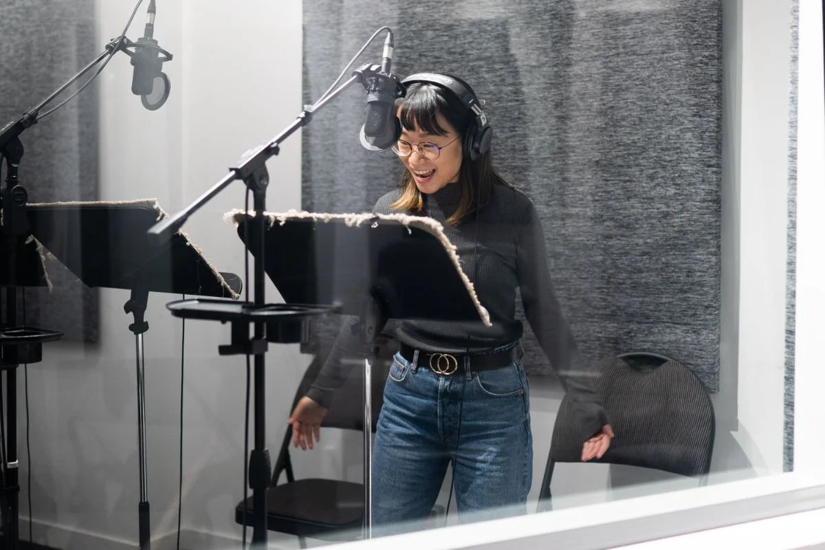 Woman performing expressively at a microphone during a broadcast narration Voice-Over class