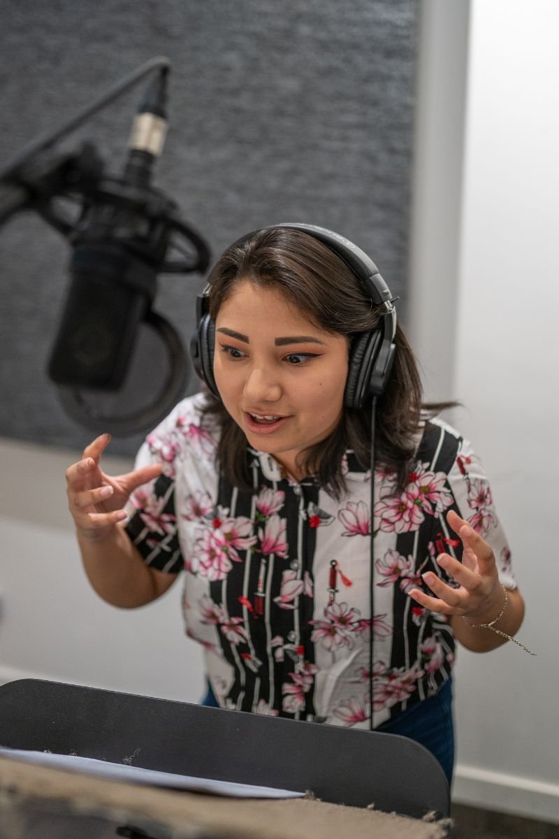 Woman wearing headphones performing at a microphone during a Commercial Voice-Over Level 2 class