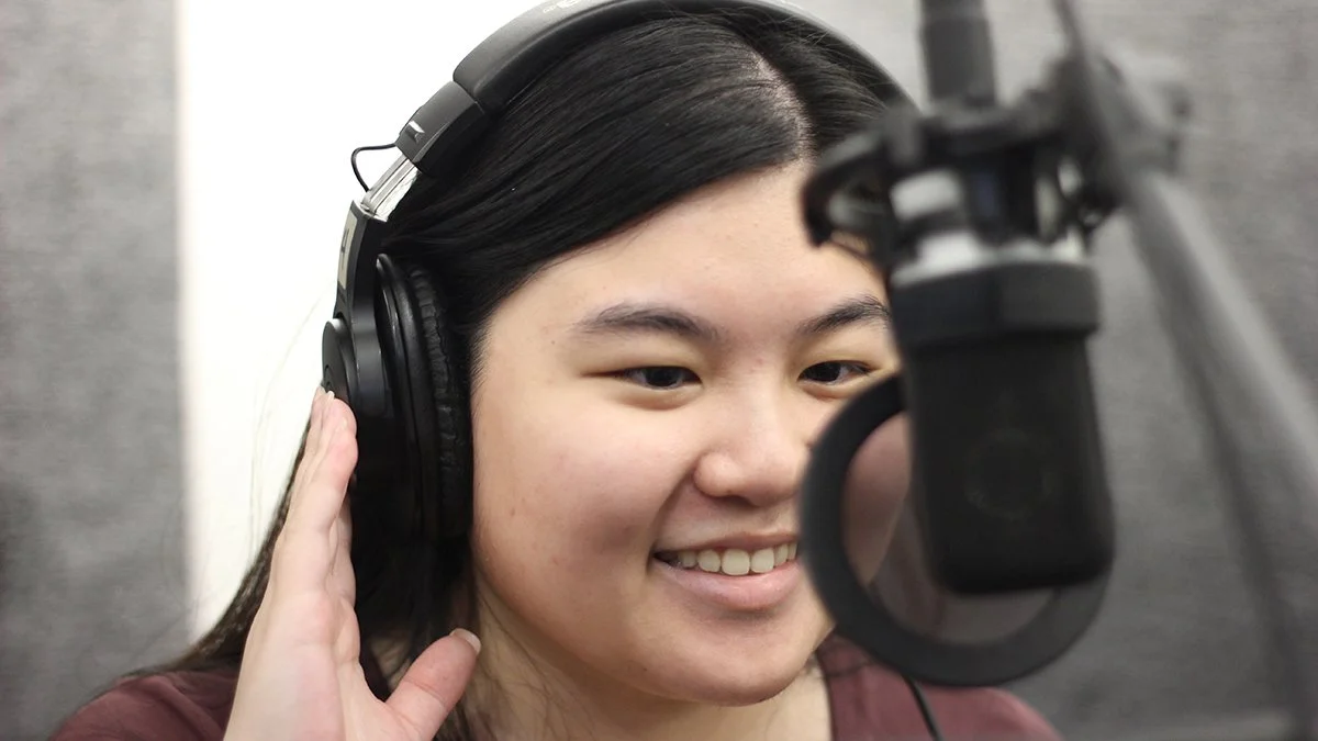 Woman wearing headphones speaking into a studio microphone during an Explore Voice-Over class