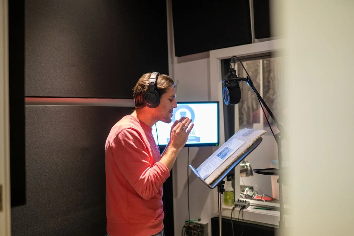 Voice actor reading from a script at a studio microphone during a corporate narration Voice-Over class