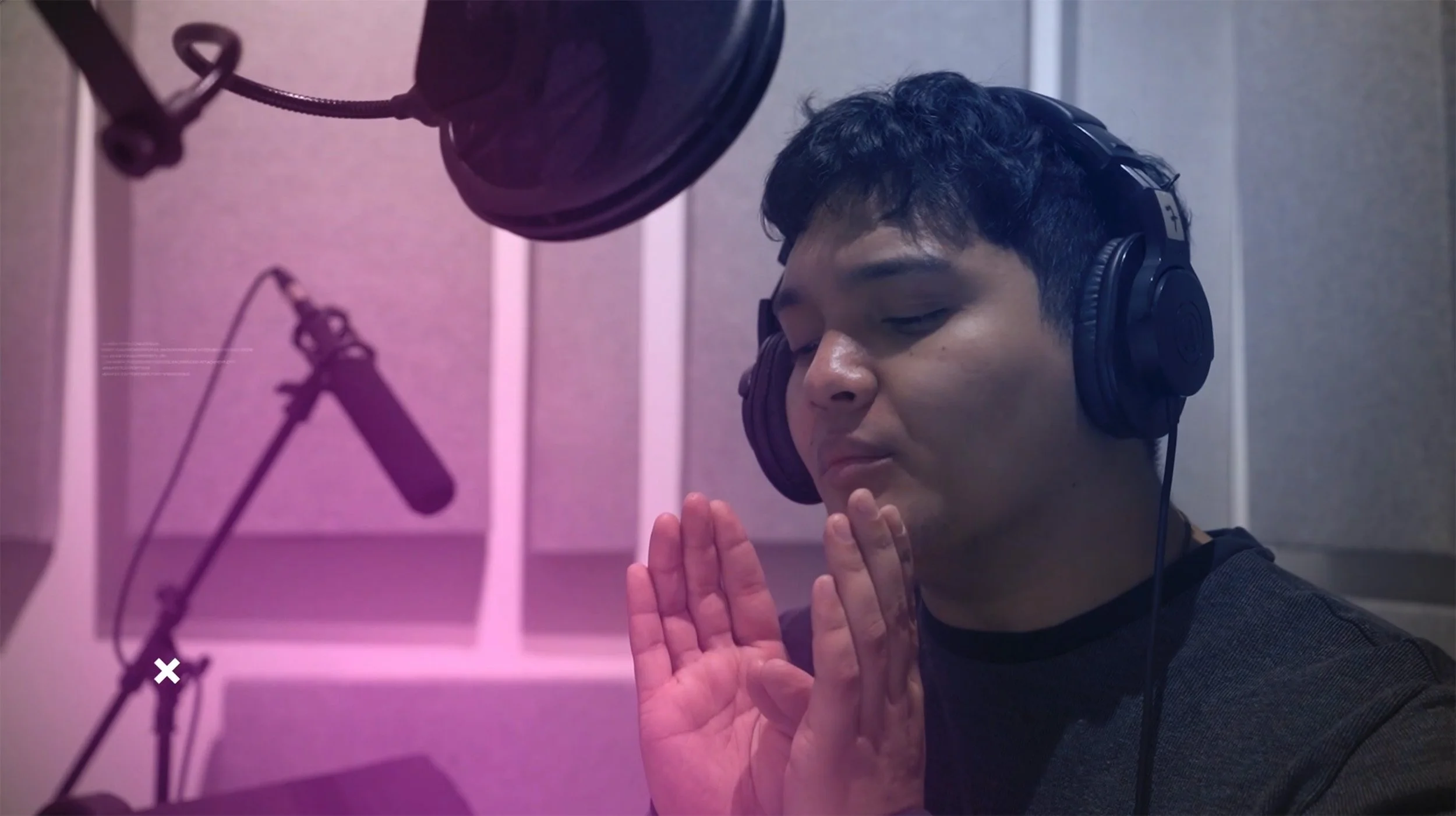 Voice-over student wearing headphones performing at a professional studio microphone during a recording session.