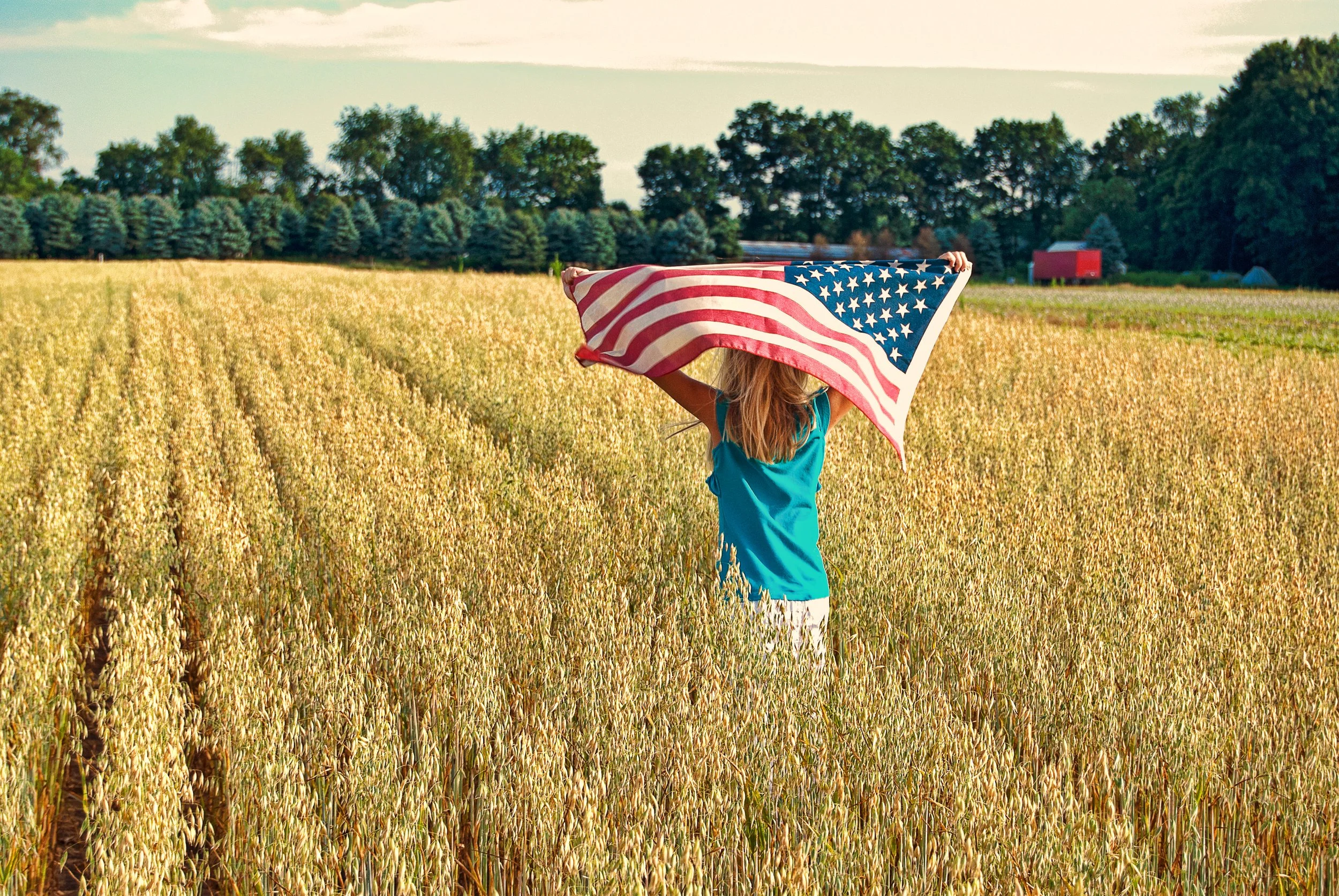 A girl runs through a Michigan field holding an American flag over her head