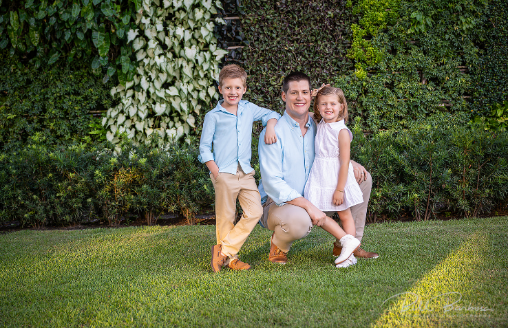 Father posing outdoors with son and daughter.