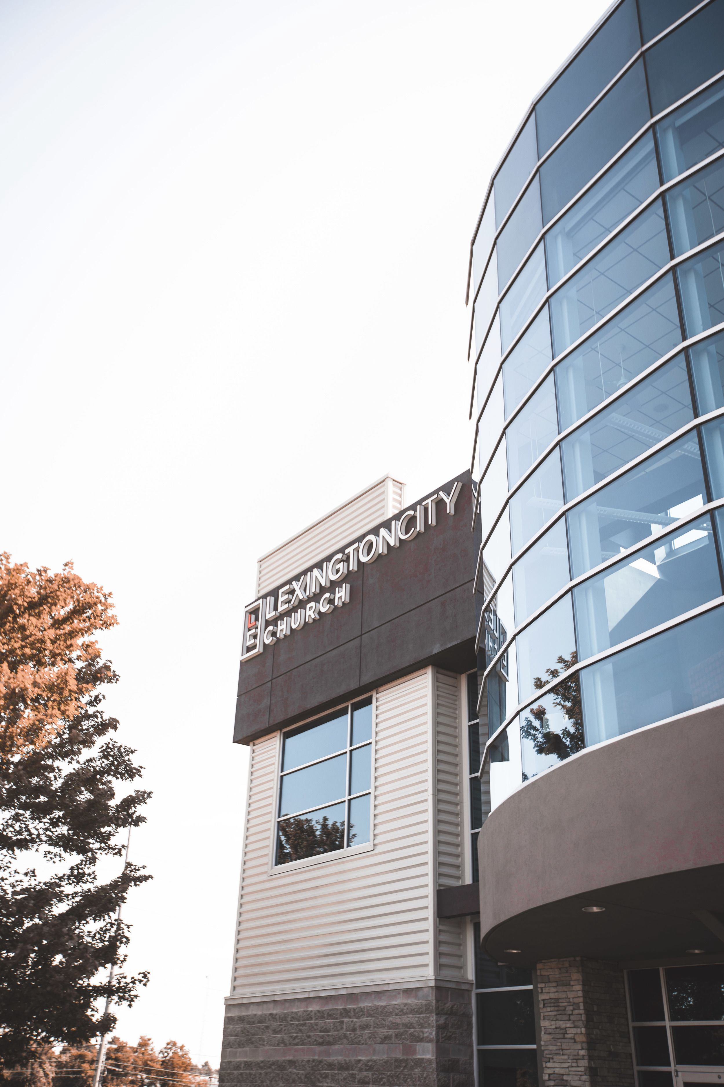 Modern building with large glass windows and a sign that reads 'Lexington City Church' on a clear day with trees nearby.