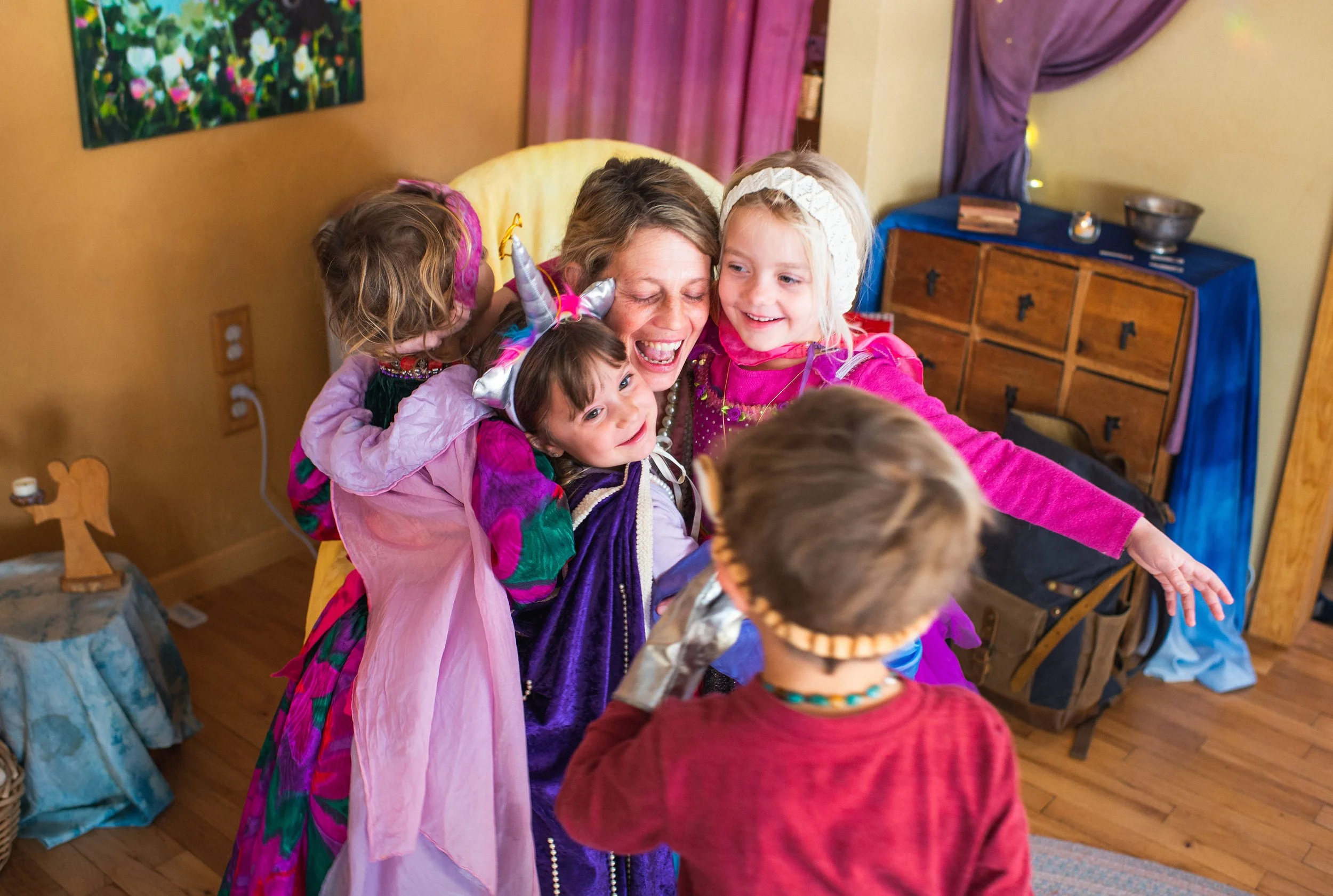 A group of children and Aiyana hug and smile together in a cozy, decorated room at Sage Programs In Boulder, CO