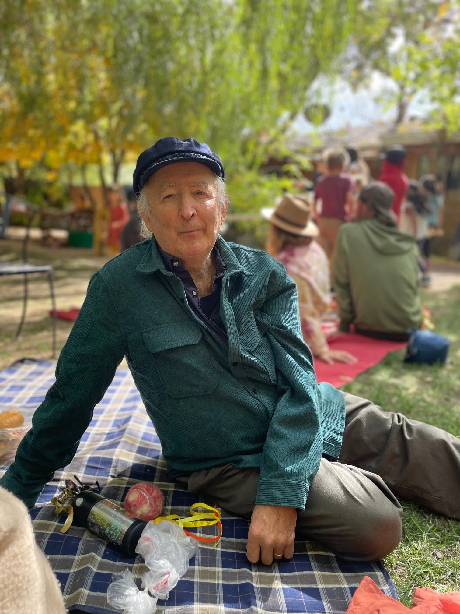 Christopher of Sage Programs in Boulder CO is sitting on the grass, wearing a dark cap and a green jacket. He is enjoying the sunshine outside on the beautiful grounds at Sage Programs.