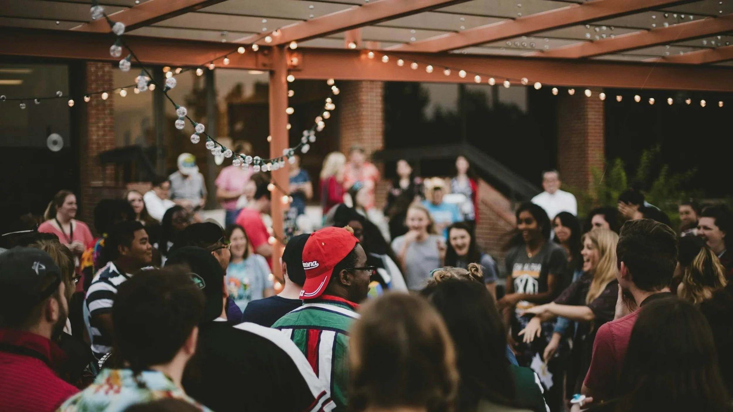 People gathered outdoors at a party or event under string lights, socializing and enjoying each other's company.