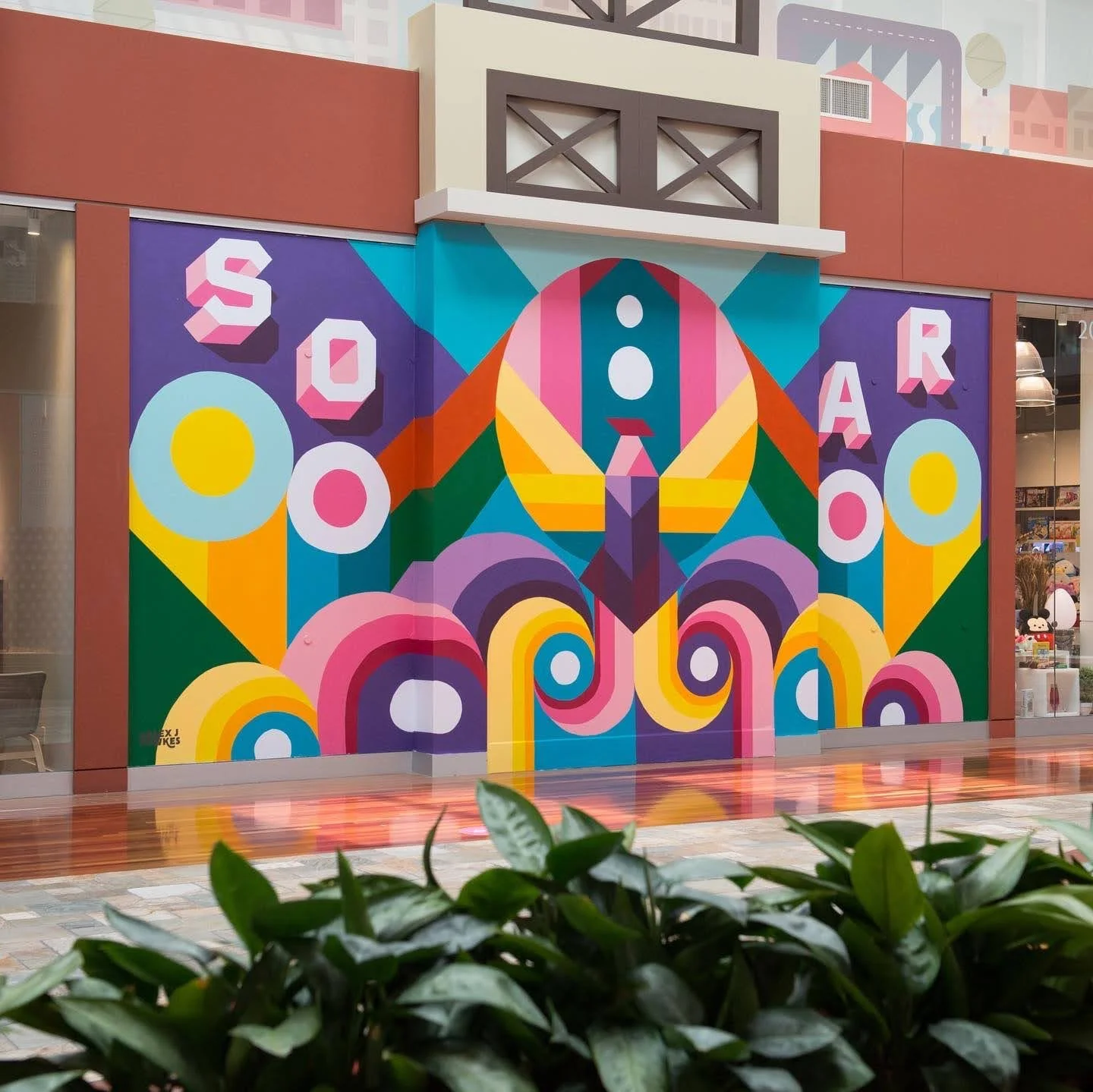 Colorful mural on a wall with the word 'SOAR' and geometric patterns in a mall setting.