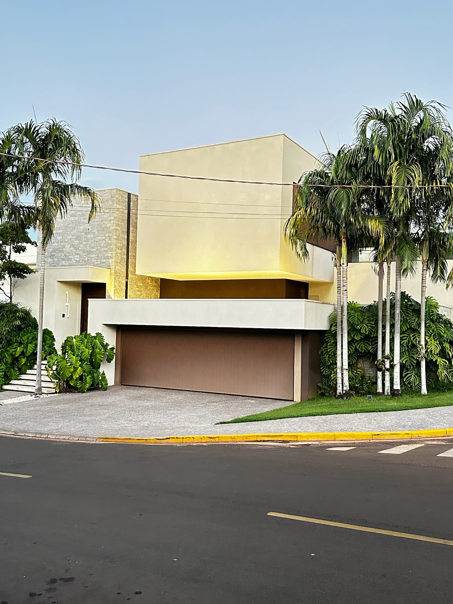 Casa moderna com fachada geométrica e palmeiras na entrada.