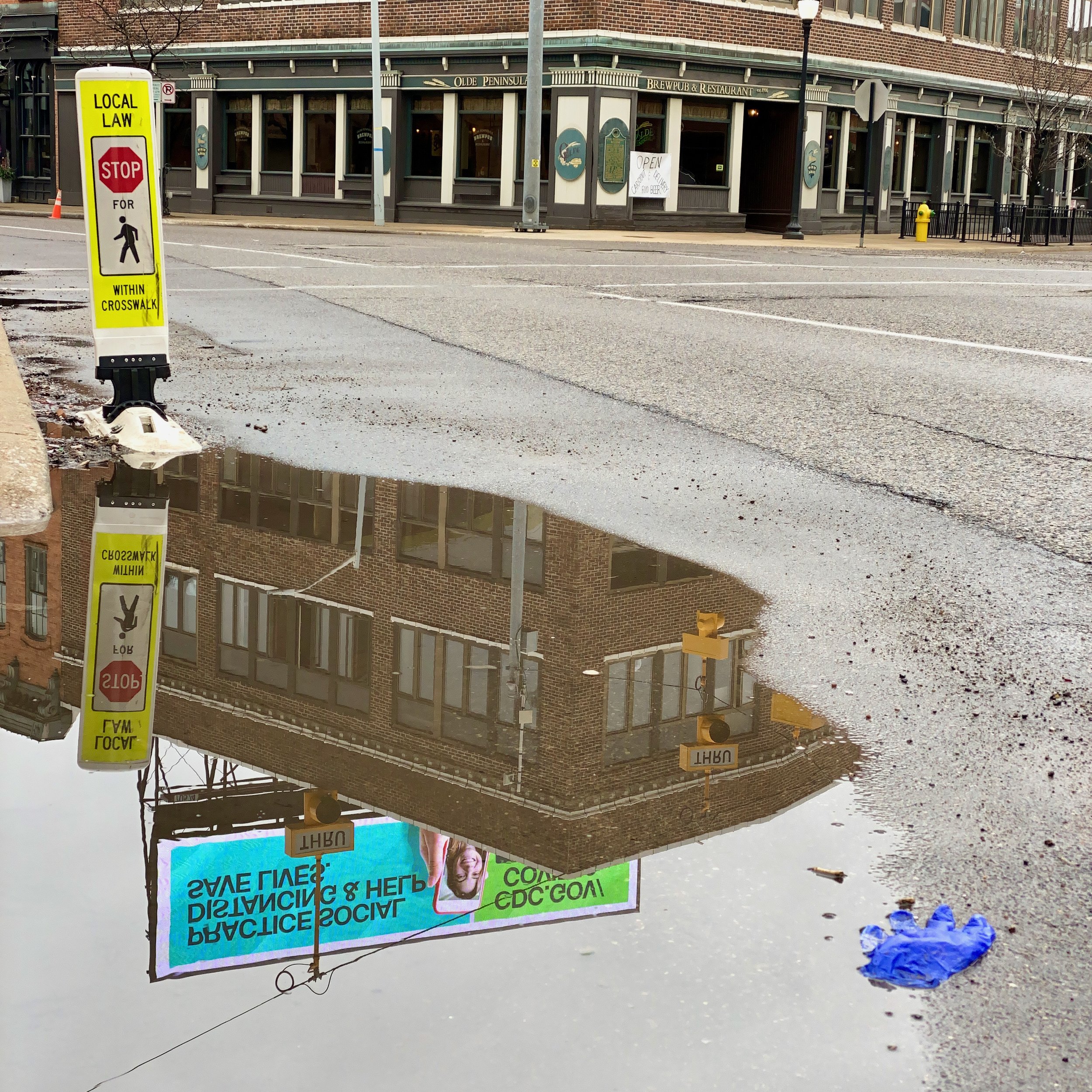 A discarded glove sits in a puddle reflecting an electronic billboard with information from the CDC on COVID-19, March 28, 2020.