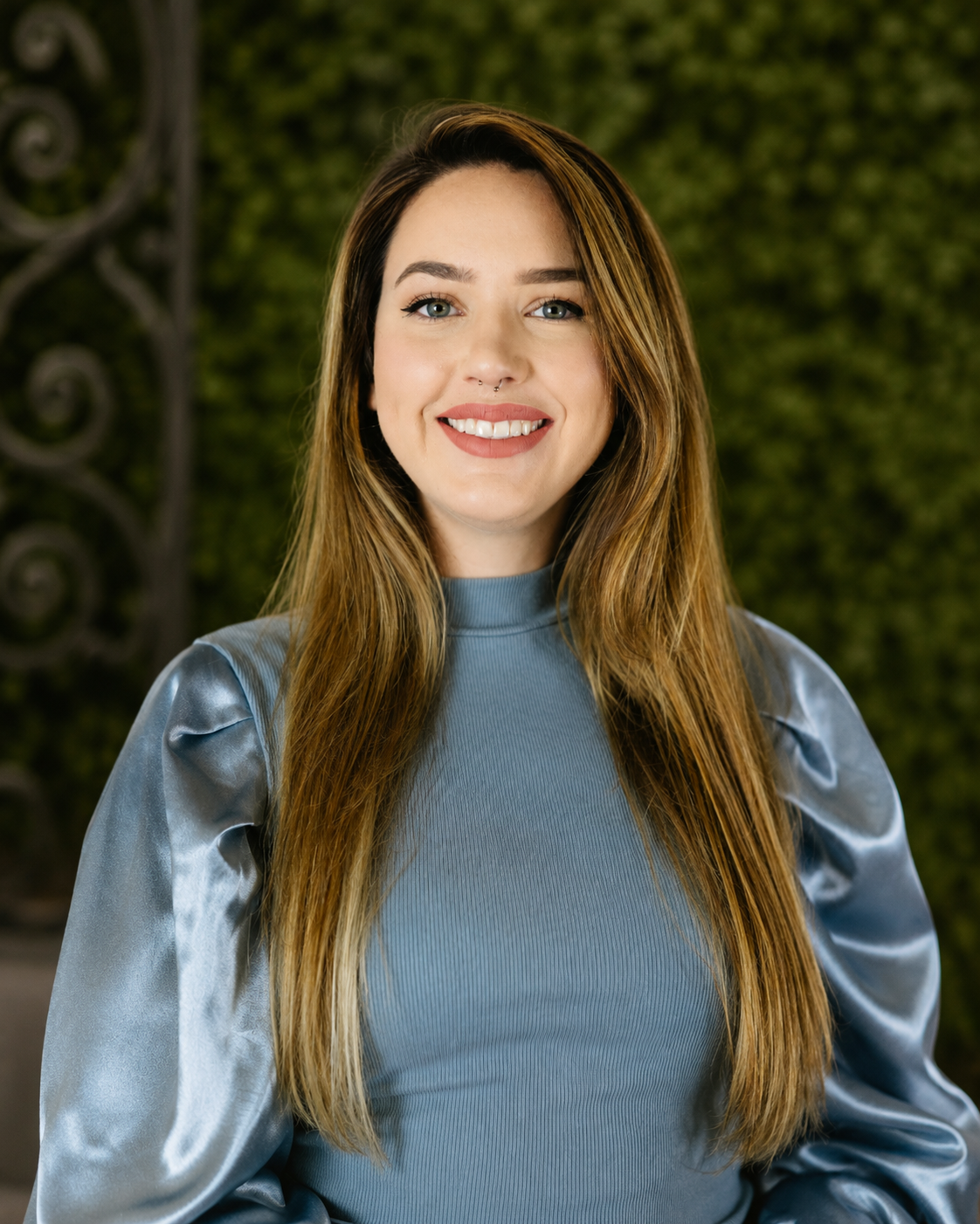 Woman in blue shirt smiling at the camera standing in front of greenery at Gabrella Manor