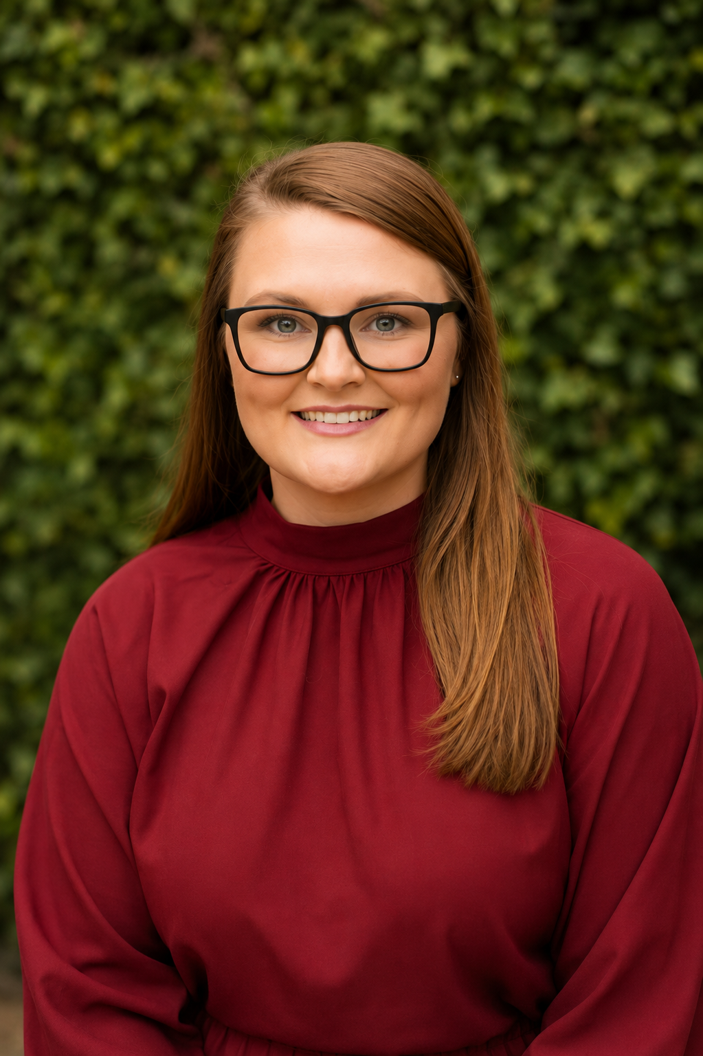 Woman with brown hair and black glasses smiling to the camera.