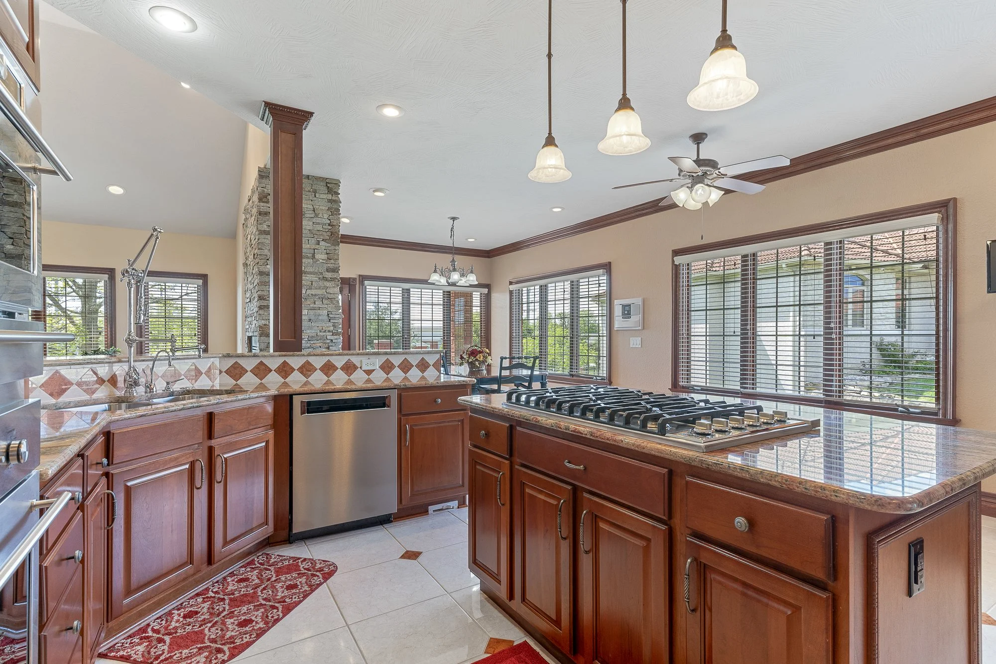Kitchen with wooden cabinets, granite countertops, large windows with blinds, a gas stove, and pendant lights hanging from the ceiling.