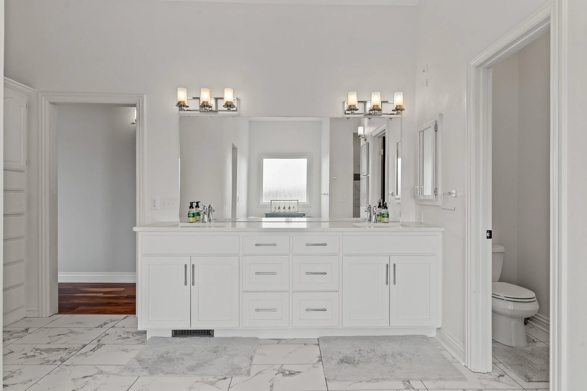 A white bathroom with vanity, marble floor tiles, and a toilet visible to the right.