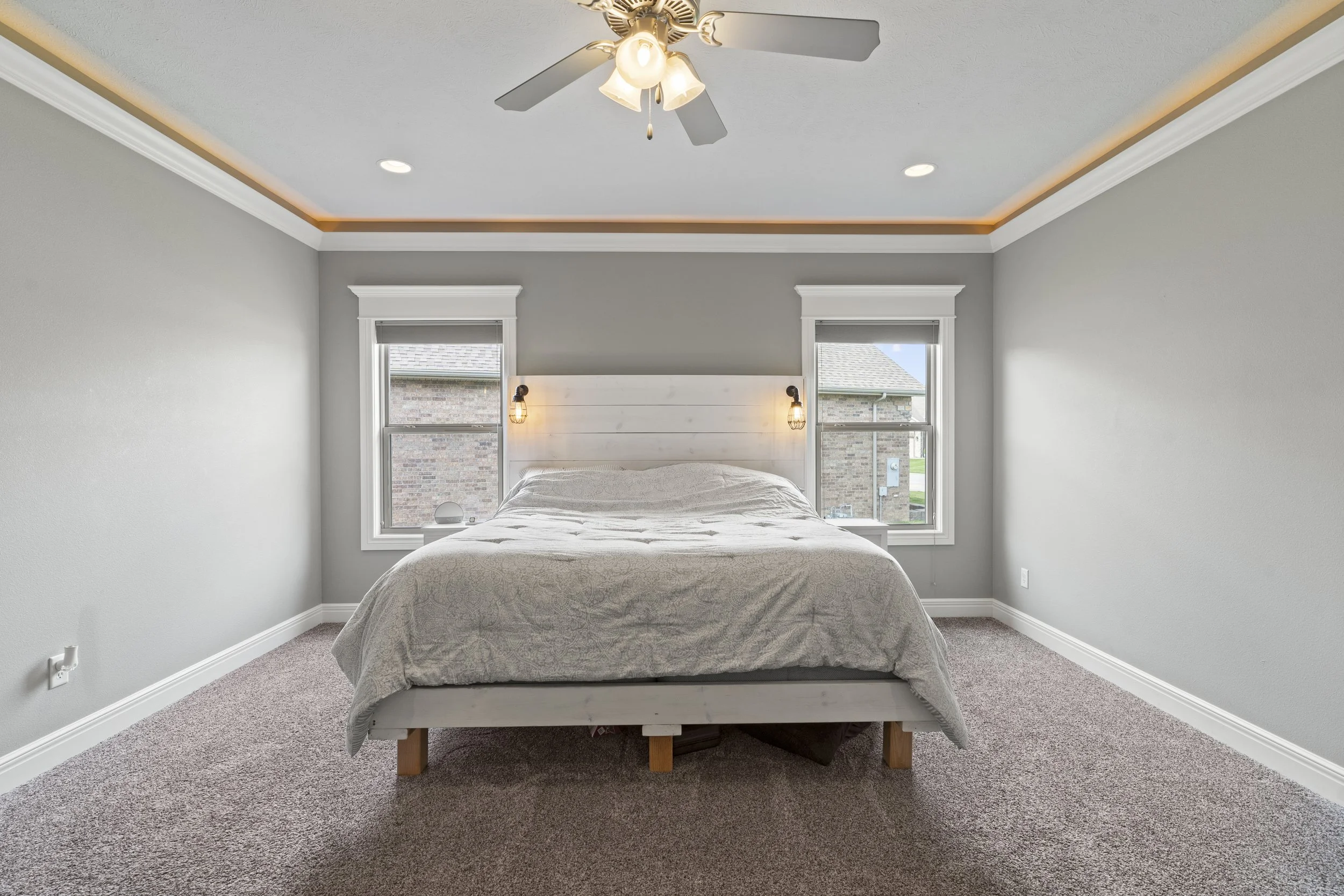 A bedroom with a bed, two windows, gray walls, a ceiling fan, and two wall-mounted lights.