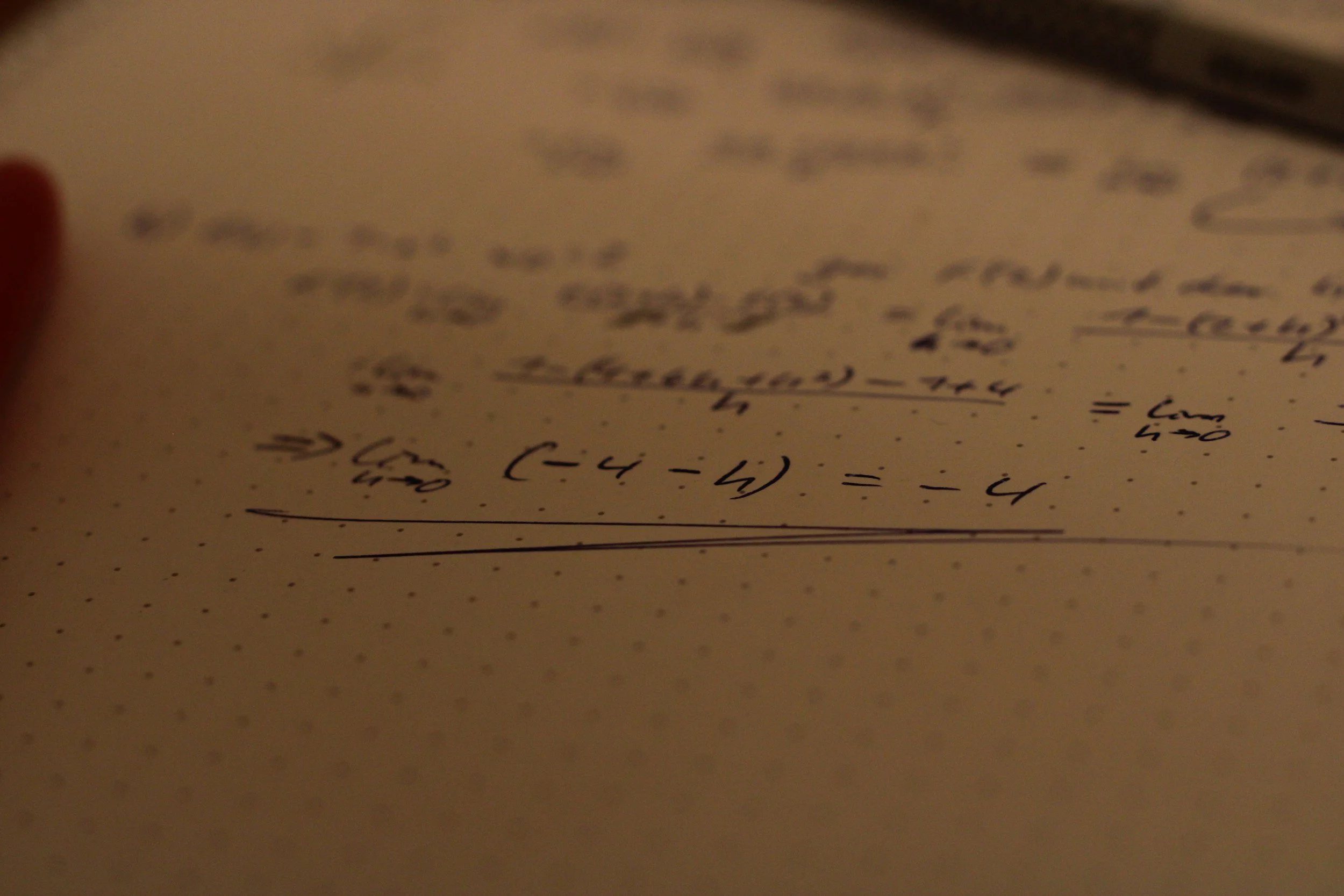 Close-up of handwritten mathematical equations on dotted paper, with emphasis on limits and algebraic expressions.