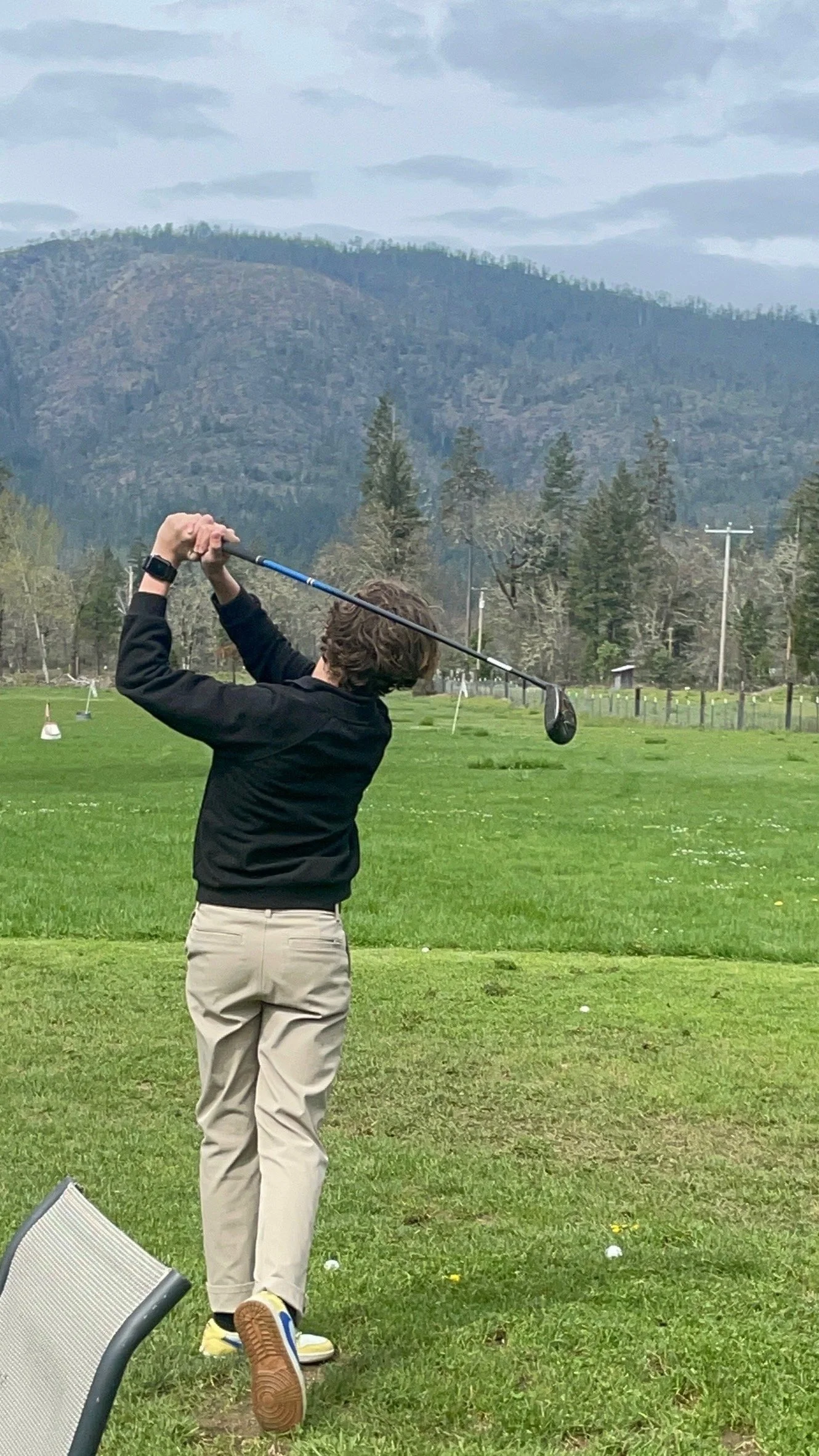 Person playing golf on a grassy field with mountains in the background
