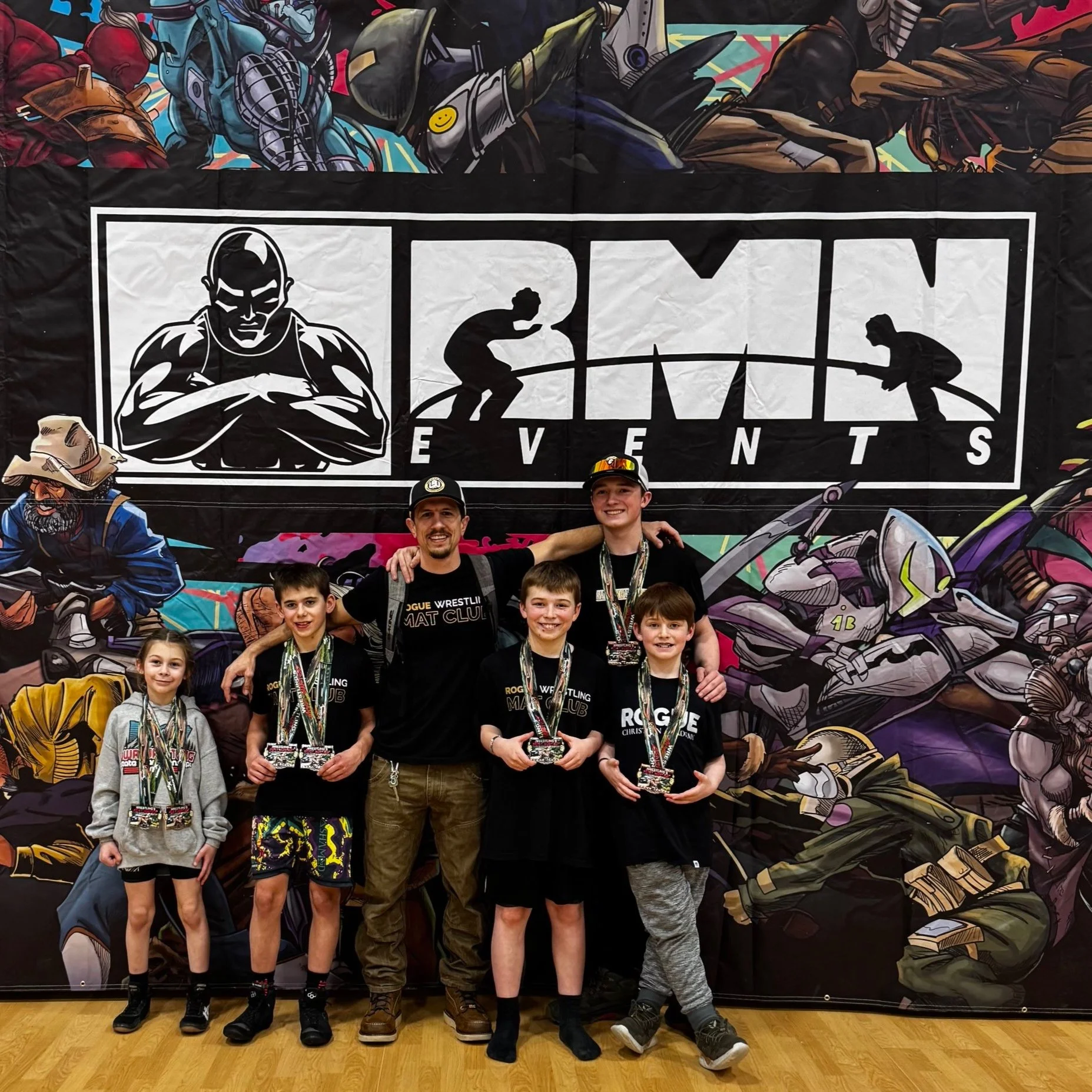 Group of young kids and two adults smiling with medals in front of RMN Events backdrop, featuring various illustrated characters.