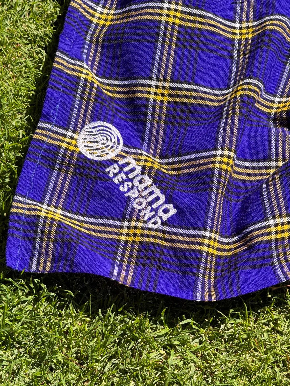 A blue plaid fabric with yellow and white lines and the words 'Rockland Resort' printed on it, lying on grass.