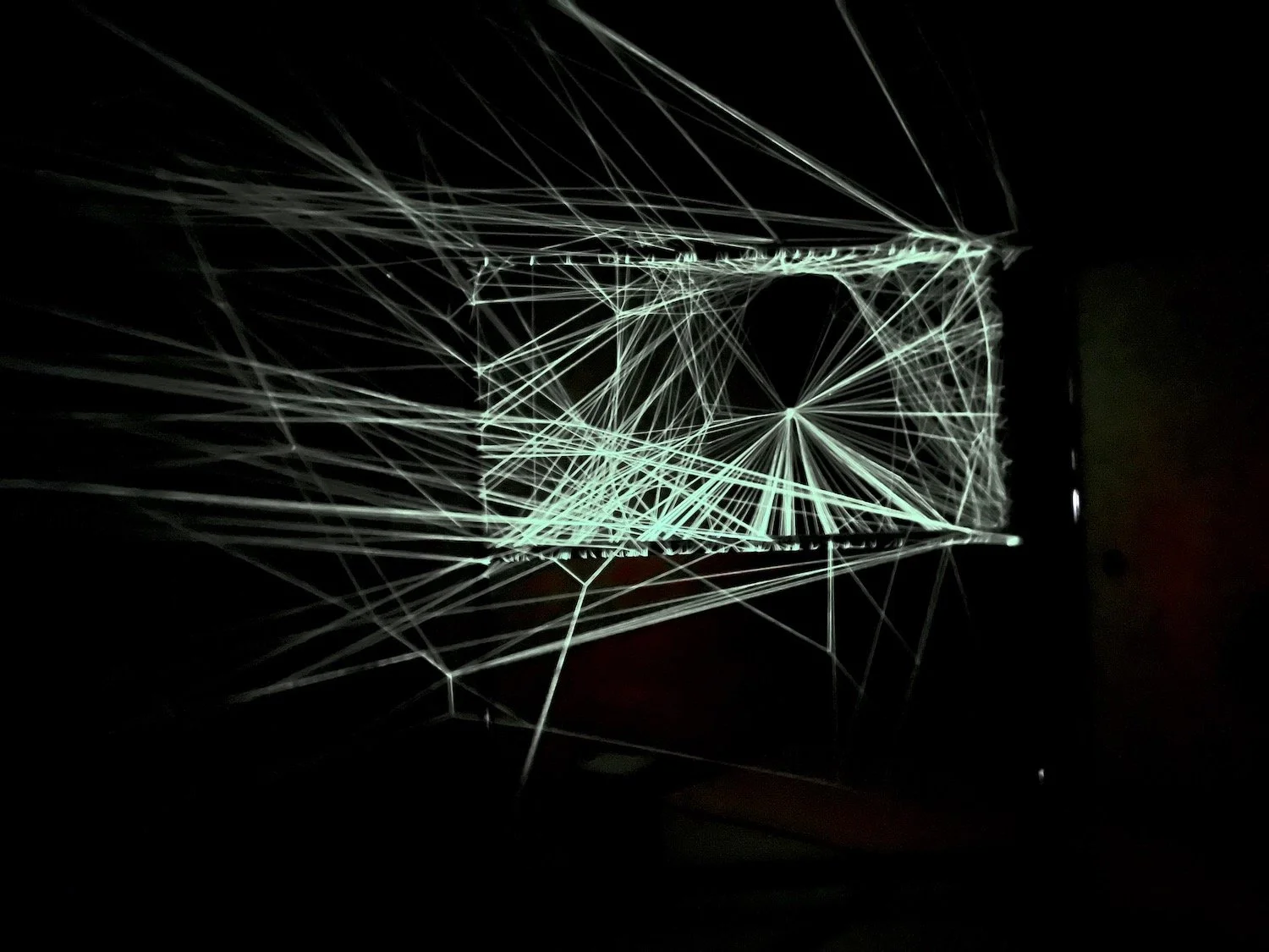 Illuminated threads forming a bright geometric network within the dark interior of the String Memory installation. / 暗い室内に光る糸が幾何学的な網状の構造をつくる《String Memory》のインスタレーション。