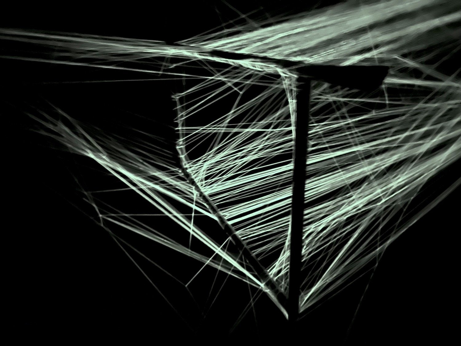 Close view of illuminated threads crossing a dark structural frame in the String Memory installation. / 《String Memory》のインスタレーションで、暗い構造体を横切る光る糸の部分。