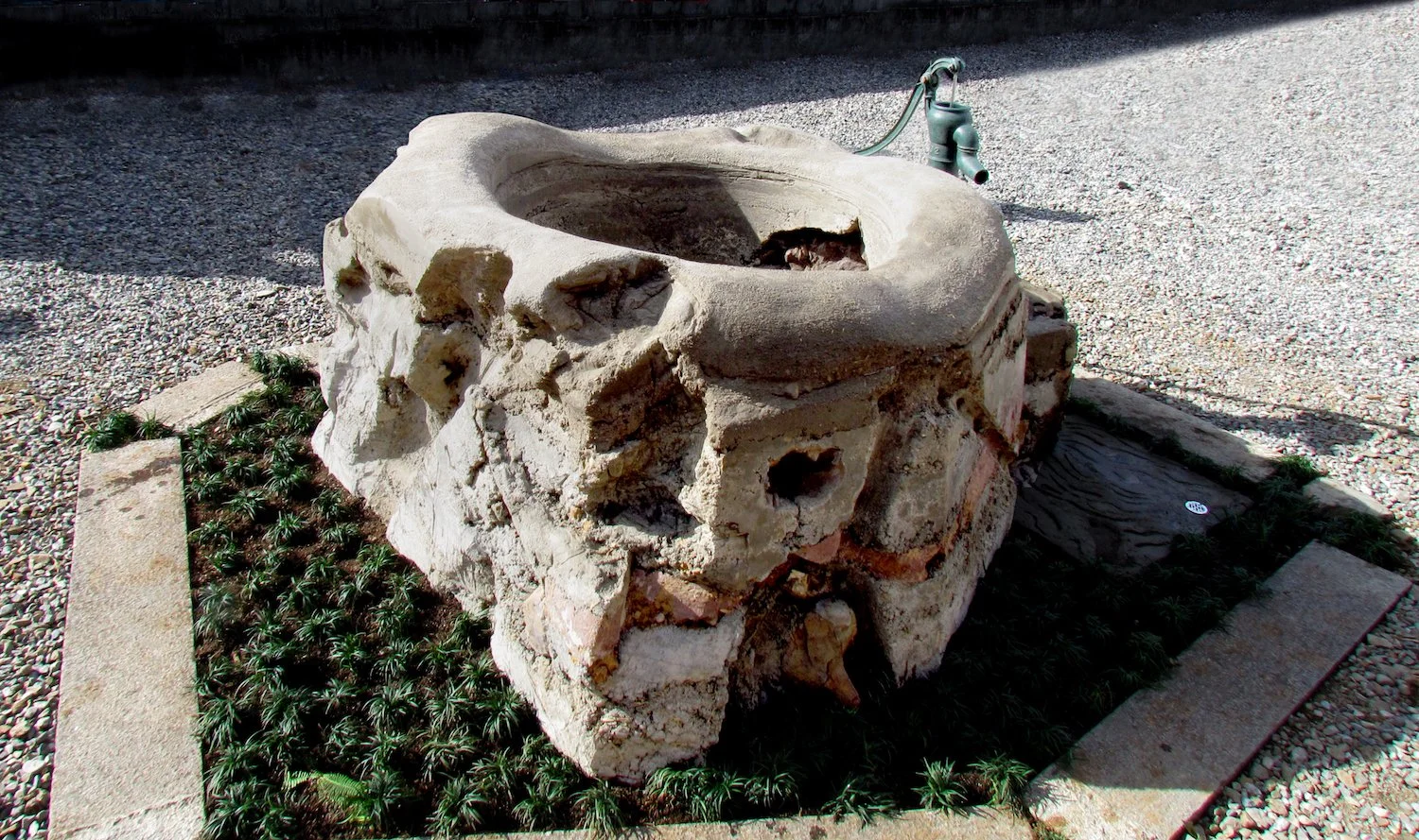 Completed sculptural earthwork with a rounded basin-like form and textured handmade surface, installed outdoors beside a hand pump. 手仕事の質感を残した丸い鉢状の造形と手押しポンプが屋外に設置された、完成後のアースワーク。