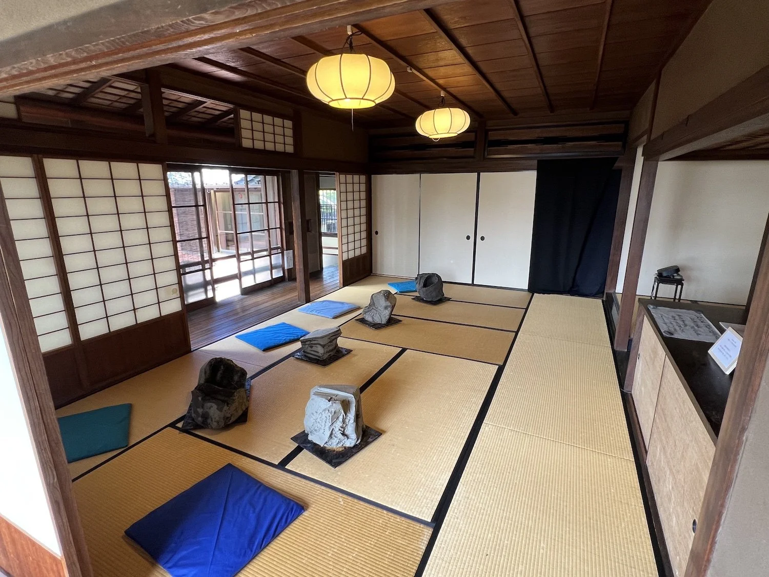Several raw-clay sculptural forms arranged across tatami mats in the Sealed by Time installation at the Former Nakano Hanroku Residence, with blue fabric in the foreground. / 旧中埜半六邸の《Sealed by Time》で、畳の上に配置された複数の生の粘土による造形と、手前に広がる青い布。