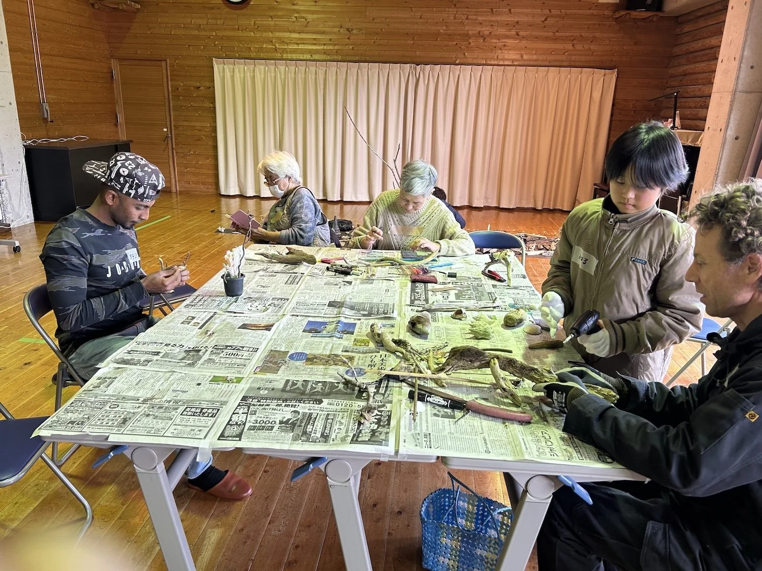 Participants work together around a table using plants and natural materials during a Himeshima WAKU WAKU workshop.姫島のWAKU WAKUワークショップで、植物や自然素材を使いながらテーブルを囲んで制作する参加者たち。