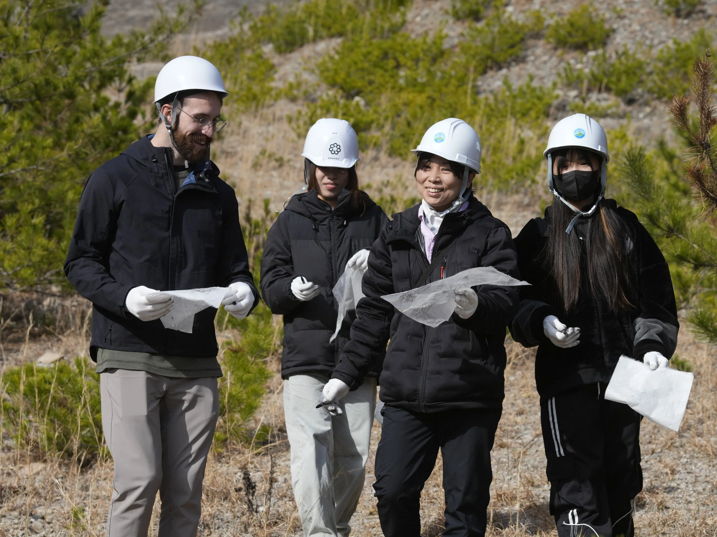 Participants wearing safety helmets walk through the former Shiroyama quarry while observing the surrounding terrain. 城山採石場跡地を歩きながら、周囲の地形や風景を観察するヘルメット姿の参加者たち。
