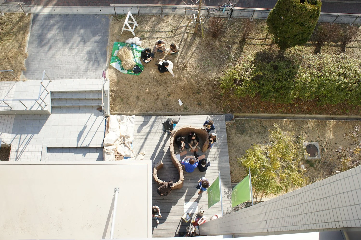 Overhead view of participants working together around the large raw-clay structure outside Clas Gallery at Nagoya University. 名古屋大学Clas Gallery屋外で、参加者が大きな生土の構造体を囲み、共同で制作している様子を上方から見た写真。