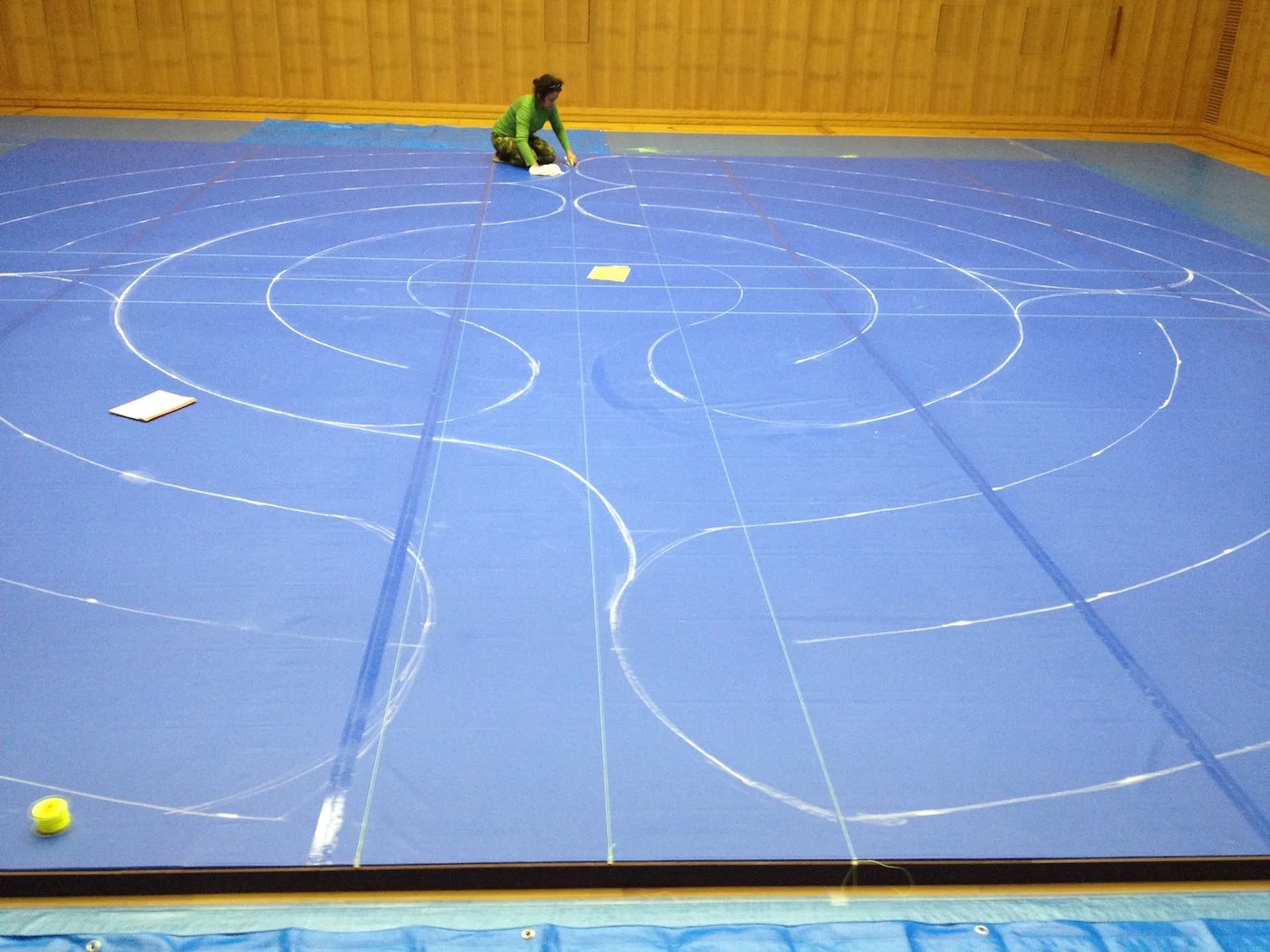 The labyrinth path marked on the blue-covered museum floor before the raw clay walls were constructed. 生の粘土による壁を築く前に、青い養生シートで覆われた美術館床面へラビリンスの道筋を描いている様子。