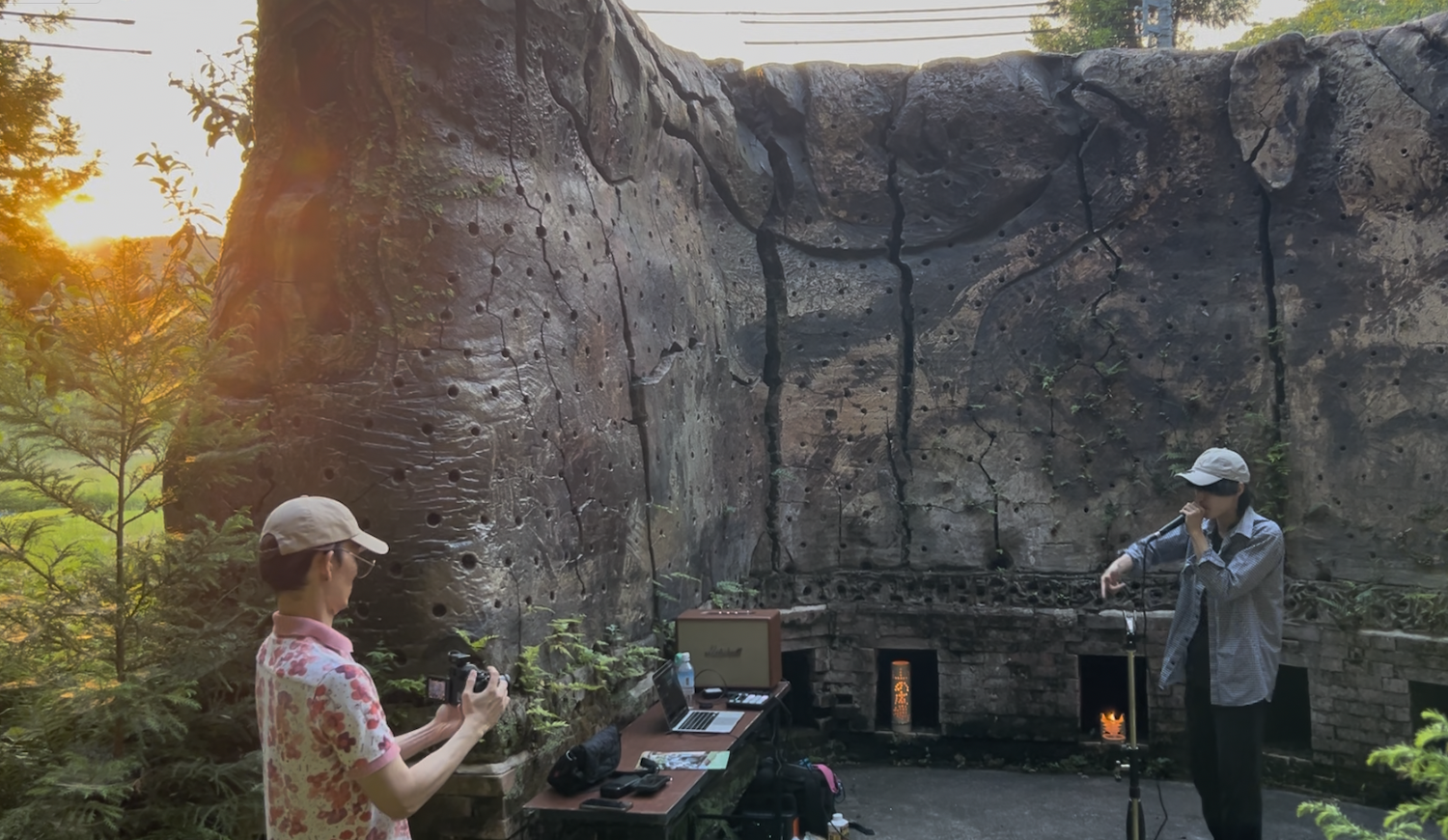 A participant speaks in front of the ceramic stage at Yama no Hiroba while others listen during an evening Open Hiroba event. 夕方の山の広場®で、焼き物の舞台を背景に話す参加者と、その話を聞く人々。