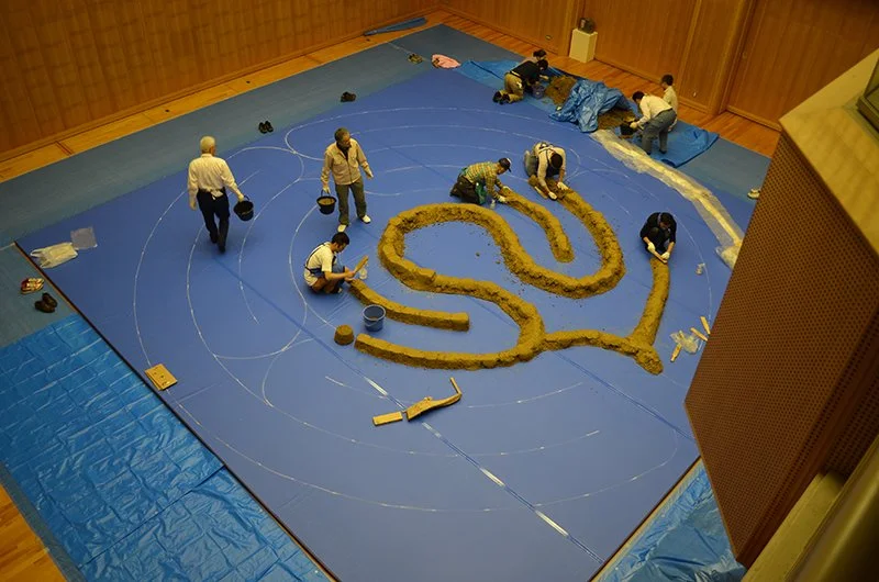 Overhead view of the TERRAM Fabulas labyrinth under construction as the earthen walls are formed along the marked path. 《TERRAM Fabulas》の制作途中を上方から見た様子。床面に描かれた道筋に沿って土の壁を形成している。