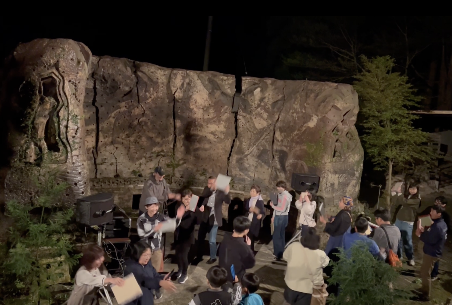 A group gathers in front of the ceramic stage at night during a 360° Open Hiroba event at Yama no Hiroba. 夜の山の広場®で、焼き物の舞台の前に集まる360°オープン広場の参加者たち。