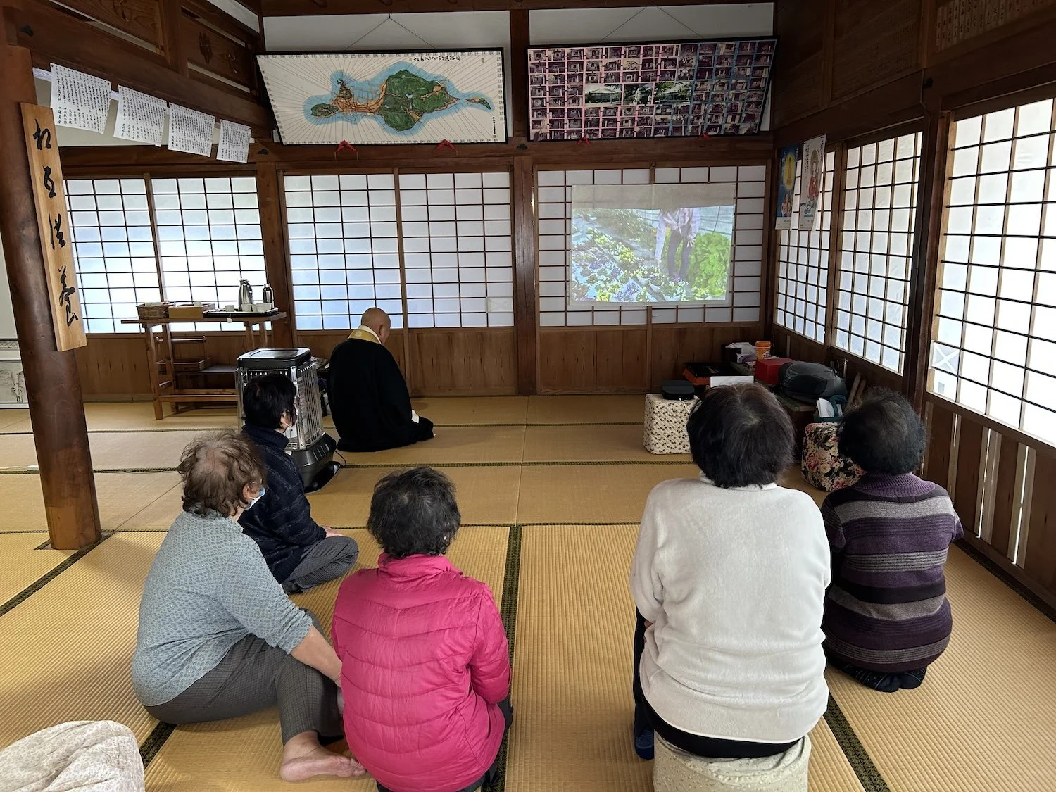 Participants sit together in a tatami room while viewing projected images during a WAKU WAKU gathering in Himeshima. 姫島のWAKU WAKUの集まりで、畳の部屋に座り、投影された画像を見る参加者たち。