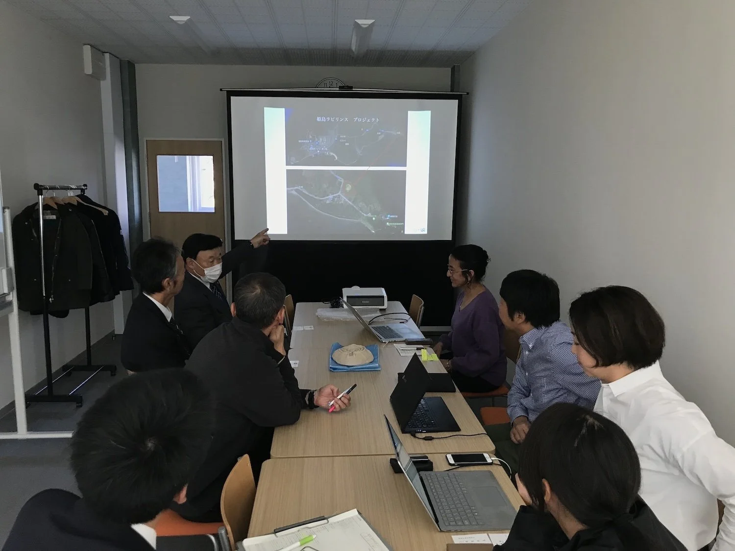 Elgueda Ward Studio presenting an early Himeshima art project proposal to members of the Himeshima Board of Education in a meeting room in November 2019.  2019年11月、会議室でエルゲダ・ウォード・スタジオが姫島村教育委員会の関係者に向けて、姫島でのアートプロジェクト初期構想を発表している様子。