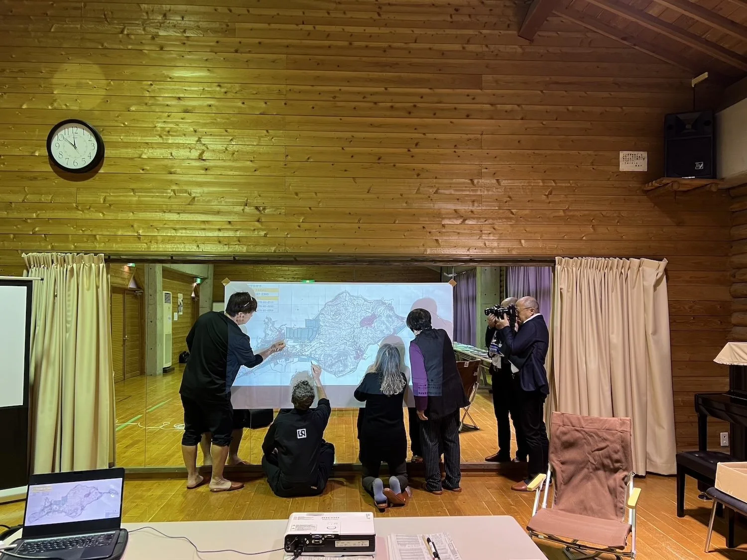 Participants gather around a projected map during an Island Atlas dialogue and documentation session in Himeshima, Oita.／大分県姫島村で、「島のアトラス」の地図を囲み、対話と記録に参加する人々。
